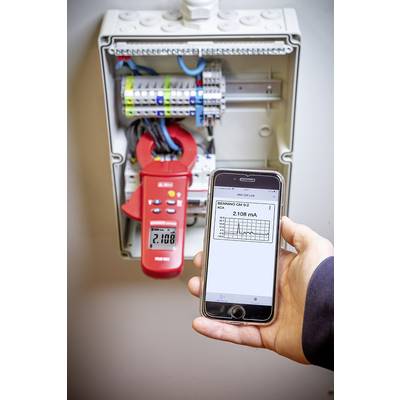Eine Person hält ein Smartphone, das eine Messung von 2108 mA von einem Gerät in einem geöffneten Verteilerkasten anzeigt.