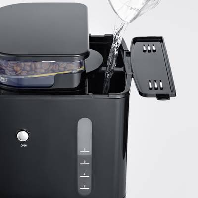 Ein Wasserkocher wird mit Wasser gefüllt. Neben der Einfüllöffnung ist ein Behälter mit Kaffeebohnen zu sehen.