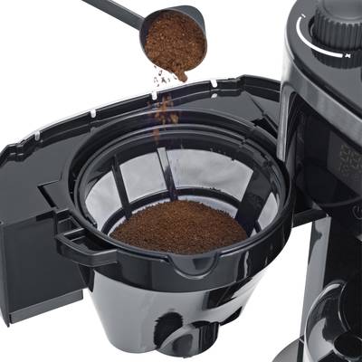 Eine Kaffeemaschine mit geöffnetem Filtereinsatz, in den gemahlener Kaffee aus einem Messlöffel eingefüllt wird.