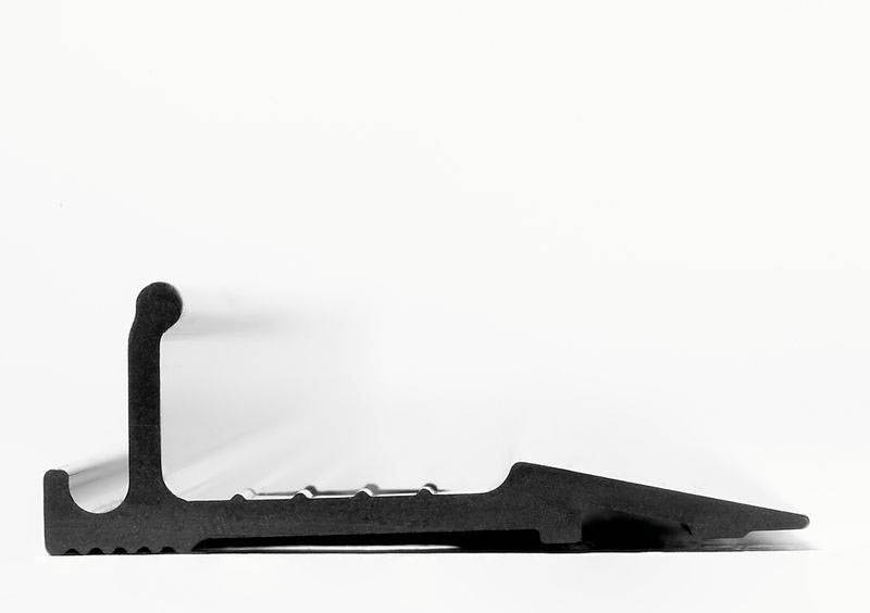 Schwarzes Metallteil, seitliche Ansicht, zeigt eine rechtwinklige Struktur mit gezackter Unterseite und einem geneigten Ende auf weißem Hintergrund.