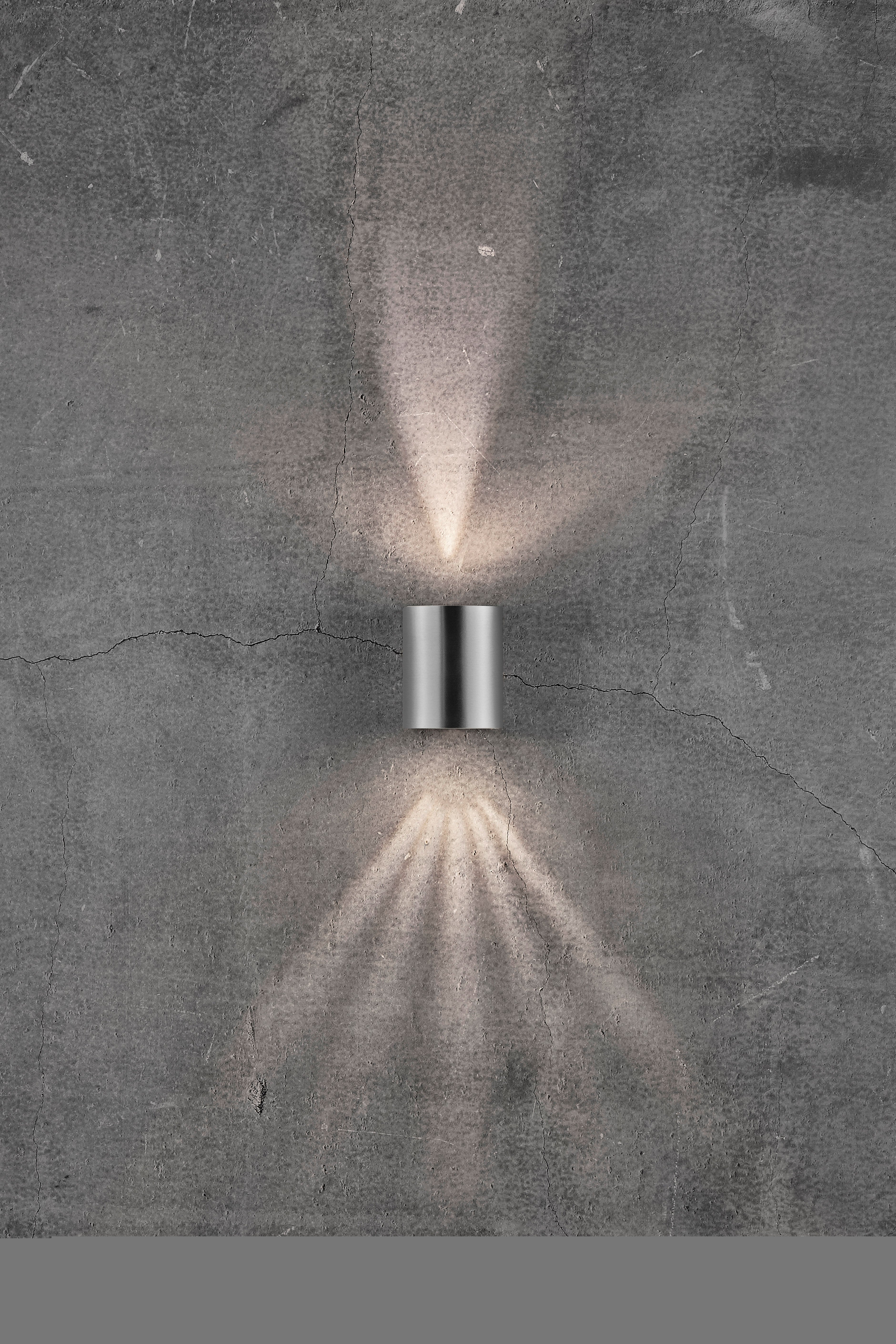 Wandleuchte auf grauer Betonwand, strahlt Licht nach oben und unten ab. Modernes Design, betont minimalistischen Stil.