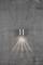 Eine silberne Wandlampe strahlt Licht nach unten auf eine graue, strukturierte Betonwand.