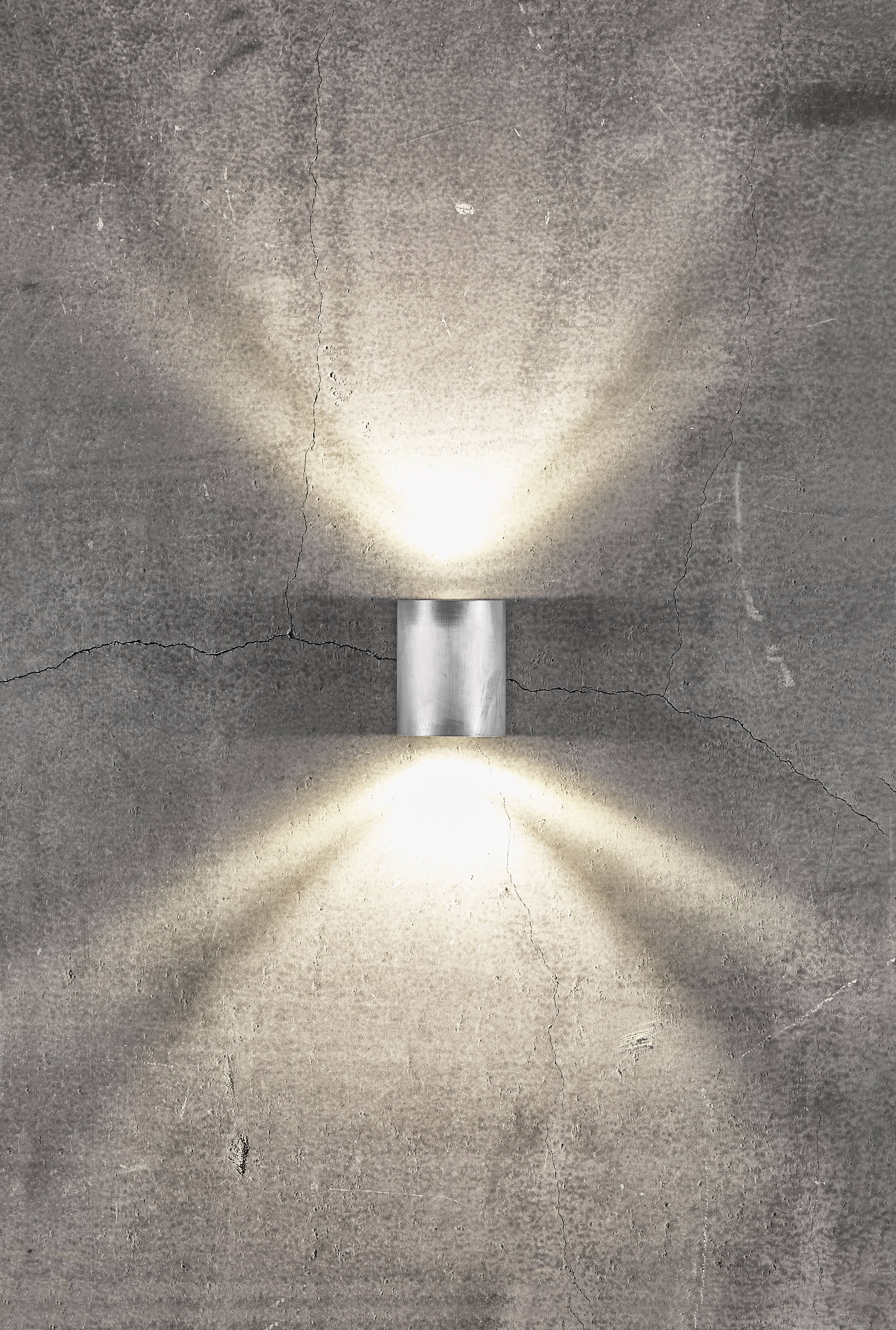 Eine Wandleuchte projiziert stimmungsvolles Licht nach oben und unten auf eine graue Betonwand.