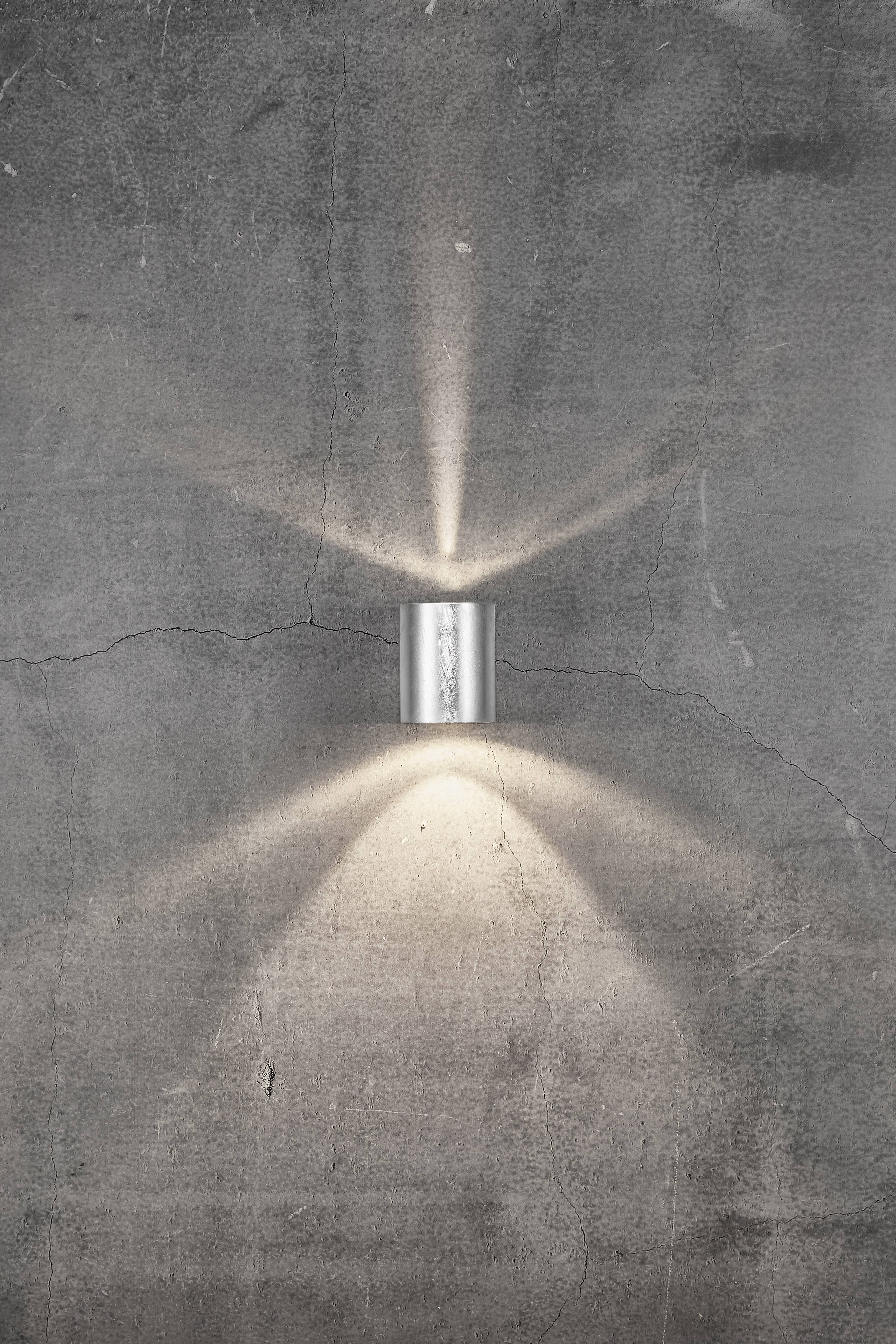Wandleuchte auf Betonwand, strahlt Licht nach oben und unten aus, erzeugt dezente Lichtkegel.