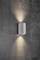 Eine zylindrische, wandmontierte Lampe in modernem Design, die sowohl nach oben als auch nach unten Licht auf einer grauen Betonwand abstrahlt.