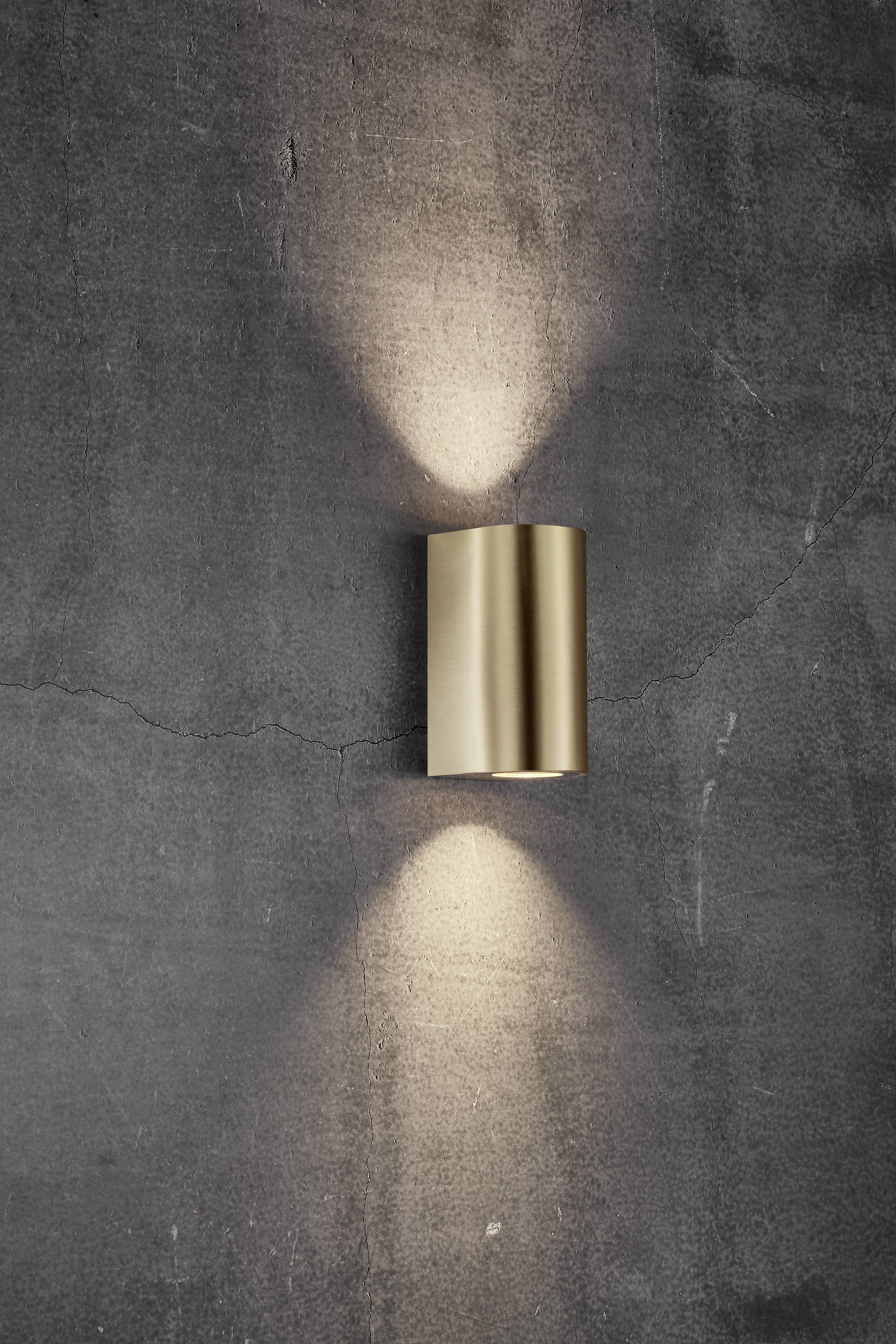 Wandleuchte in Gold an grauer Wand, strahlt Licht nach oben und unten.