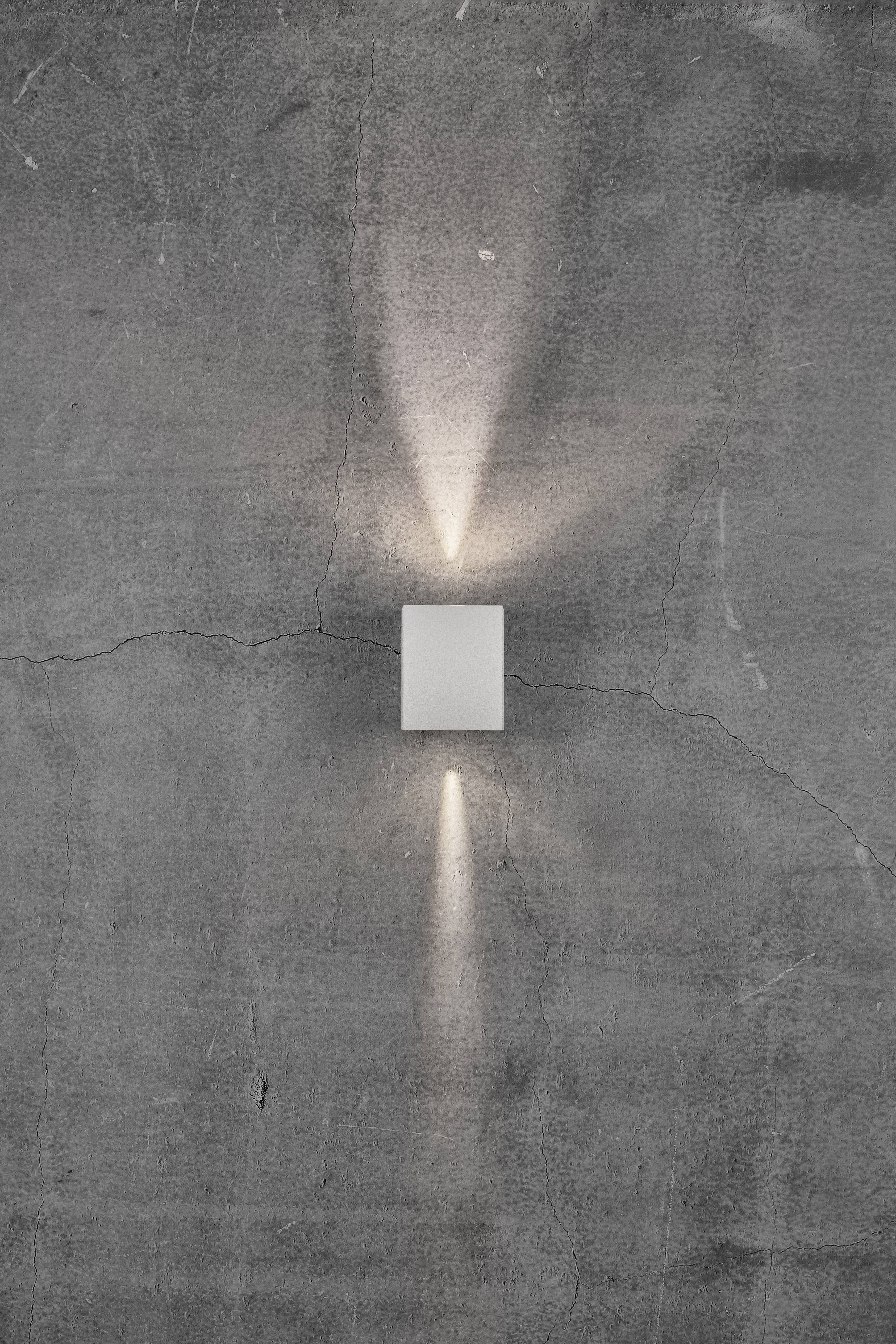 Eine Wandleuchte strahlt weiches Licht nach oben und unten auf eine raue, graue Wand.