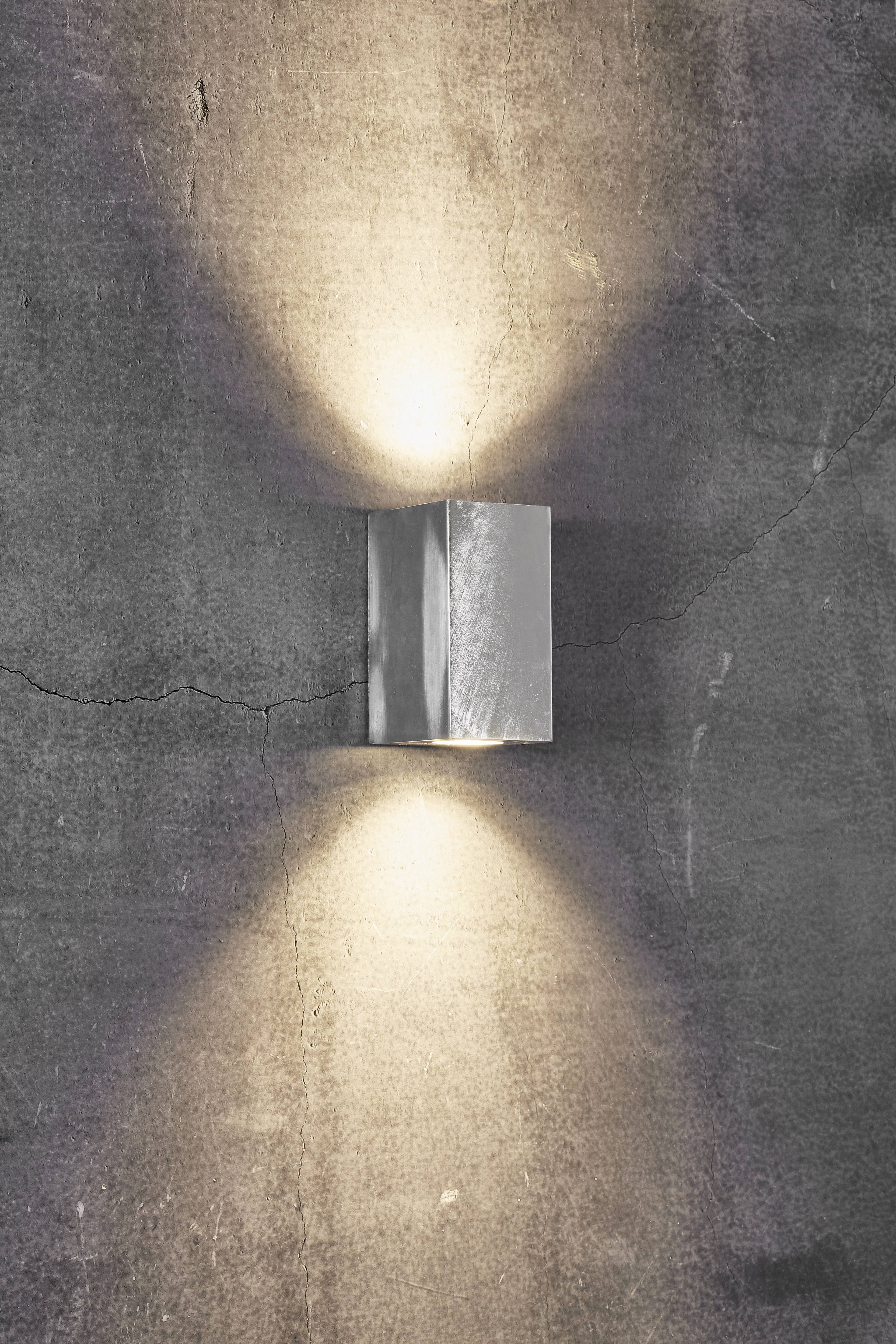 Eine Wandlampe wirft warmes Licht nach oben und unten auf eine raue Betonwand, schafft eine einladende Atmosphäre.