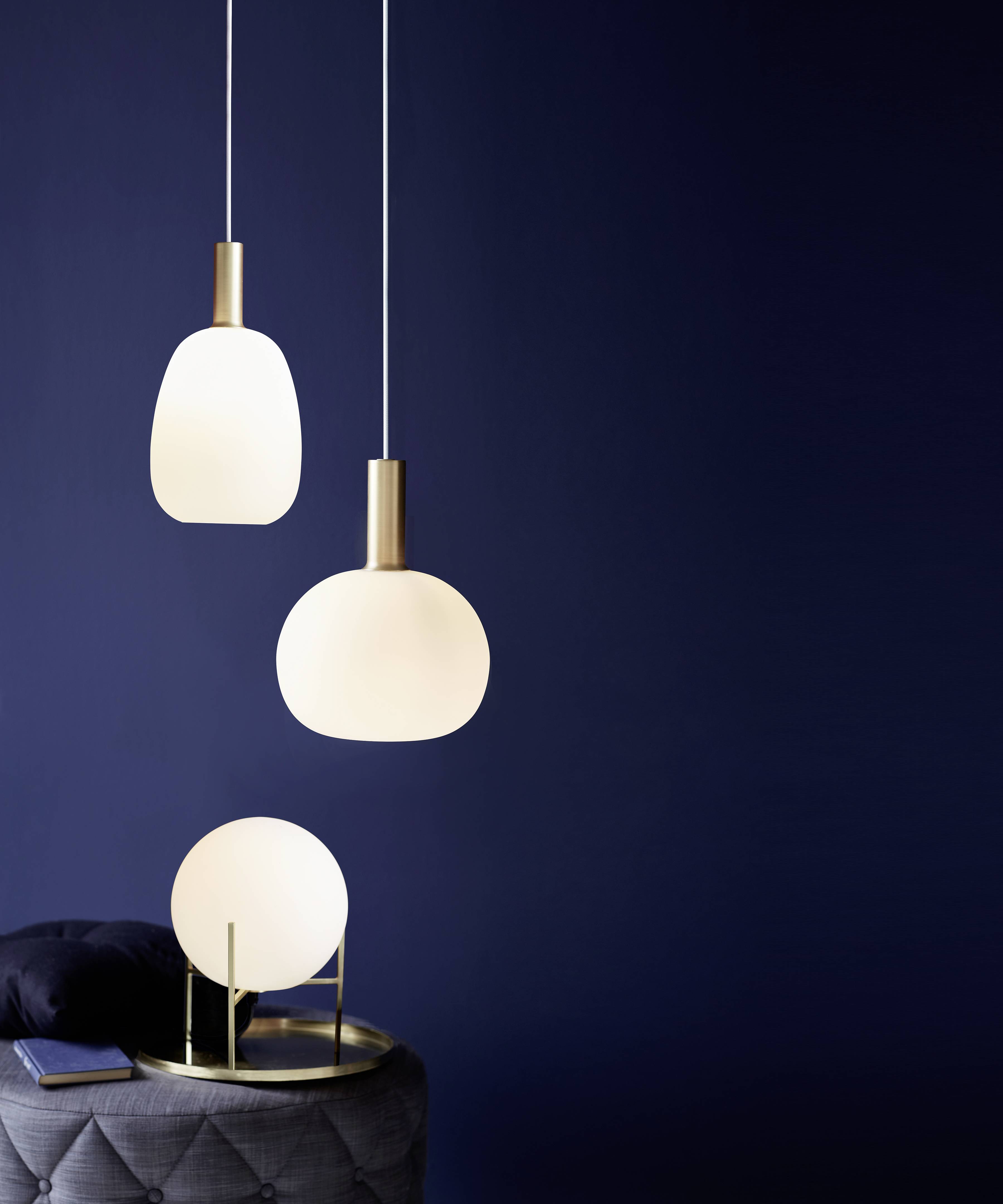 Drei moderne, weiße Hängelampen vor dunkelblauem Hintergrund. Rechts ein runder Beistelltisch mit Kissen und Lampe.