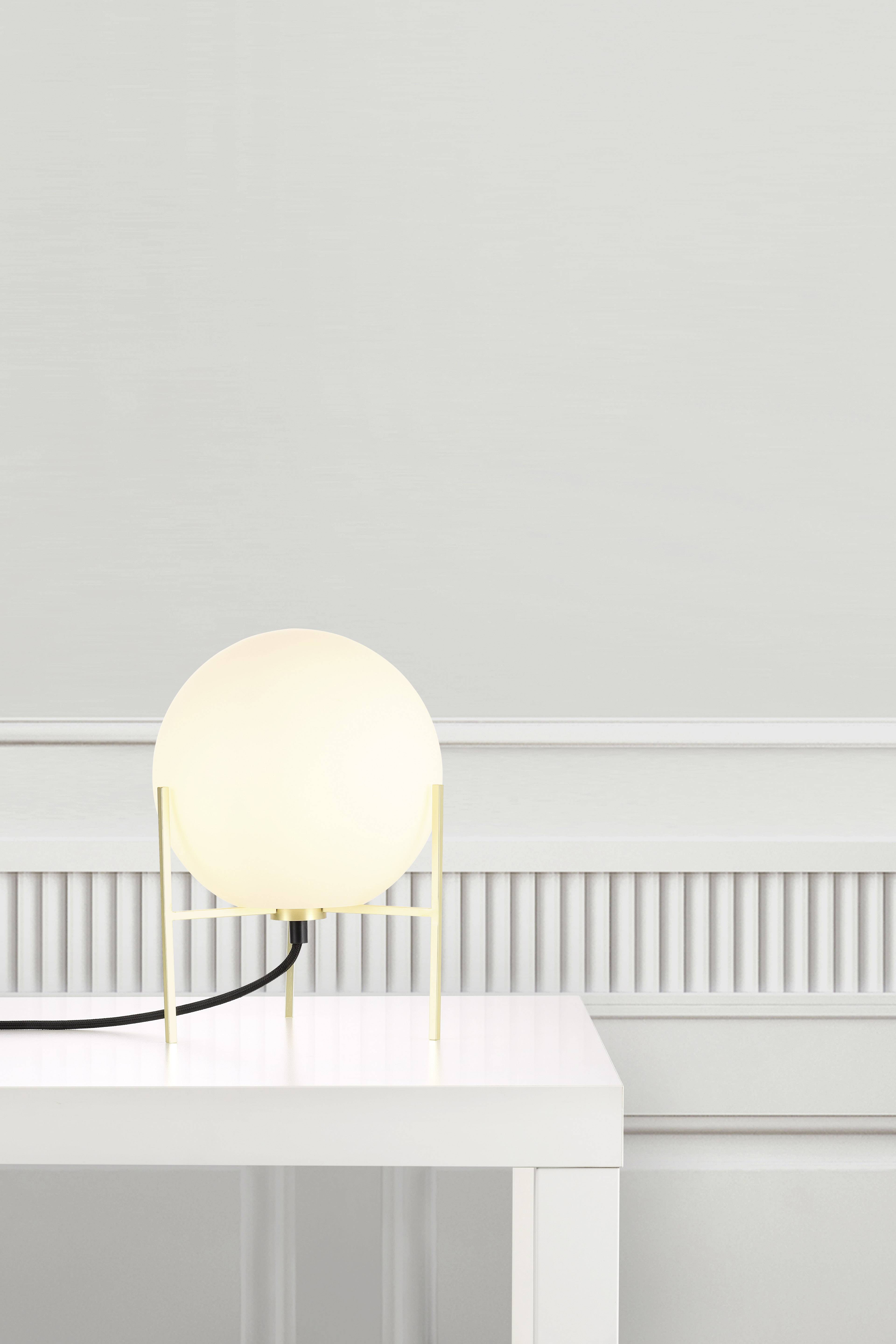 Kleine Tischlampe mit kugelförmigem Lampenschirm auf einem weißen Tisch vor einer hellgrauen Wand.