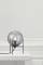 Eine moderne Tischlampe mit kugelförmigem, transparentem Schirm steht auf einem weißen Tisch. Sie strahlt warmes Licht aus.
