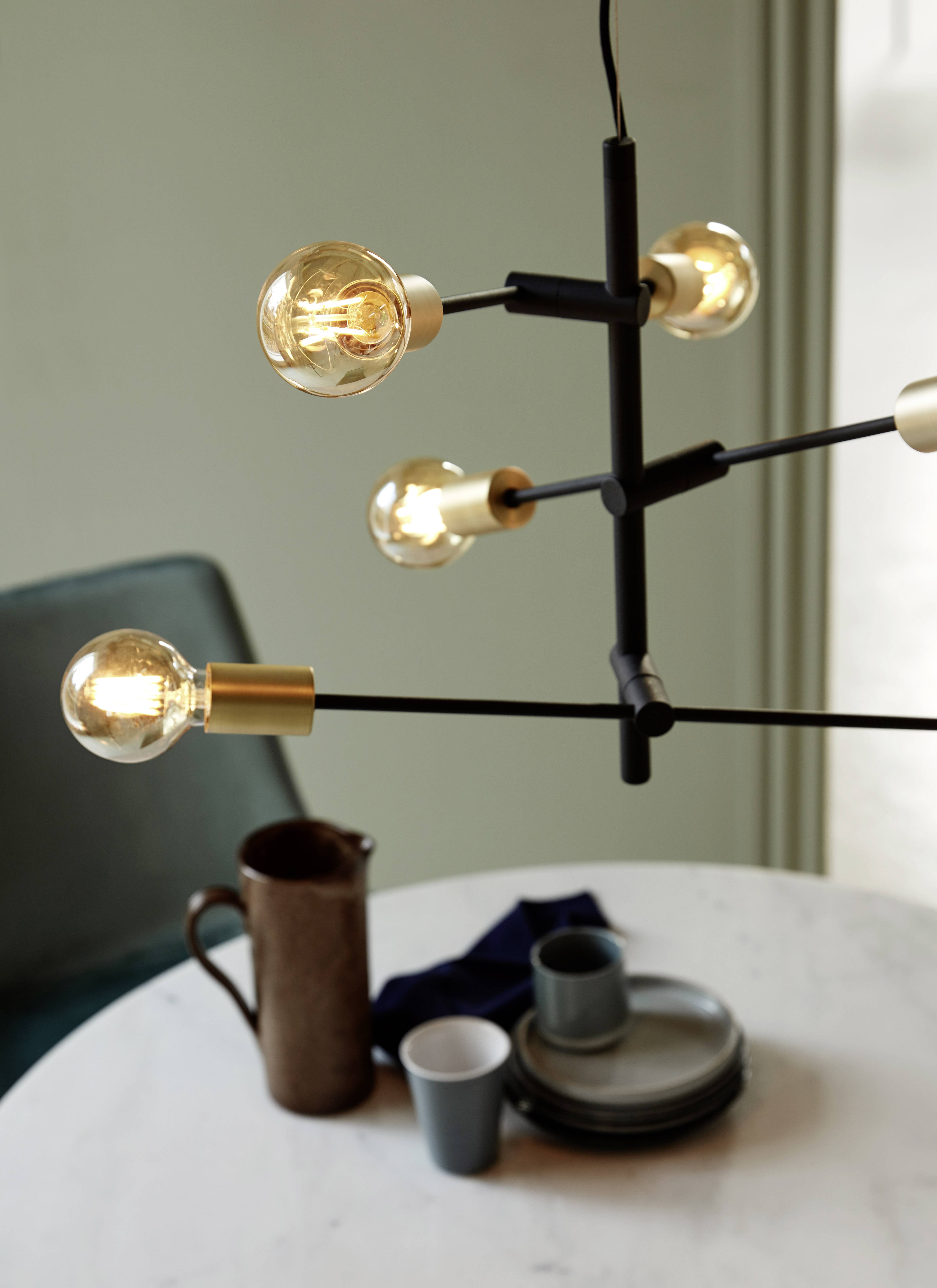 Eine moderne Hängeleuchte mit mehreren Glühbirnen über einem Tisch, auf dem Geschirr und eine Kaffeekanne stehen.
