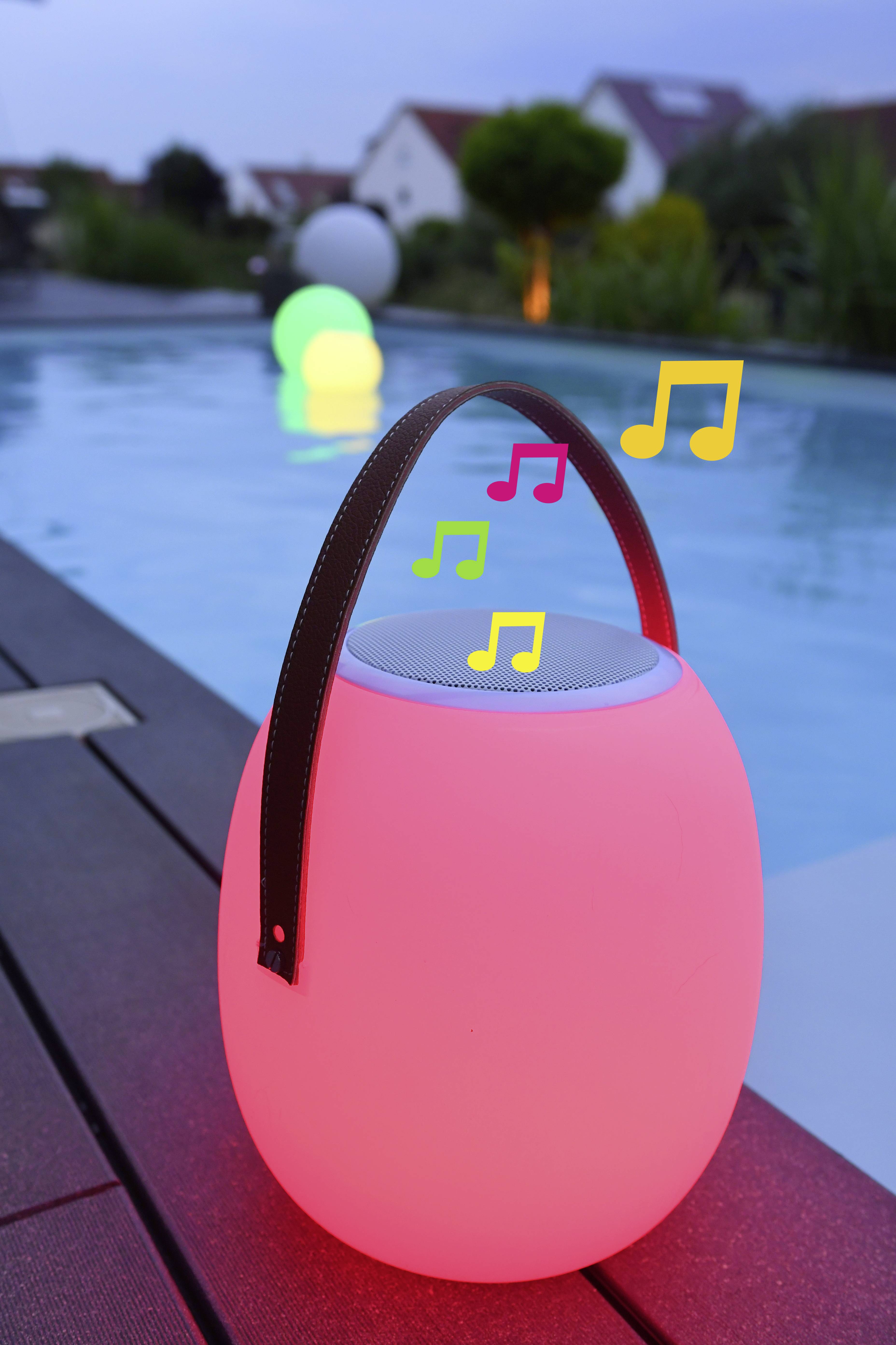 Ein runder, rosa leuchtender Lautsprecher mit Musiknoten-Symbolen steht am Poolrand. Im Hintergrund schwimmen beleuchtete Kugeln im Wasser.