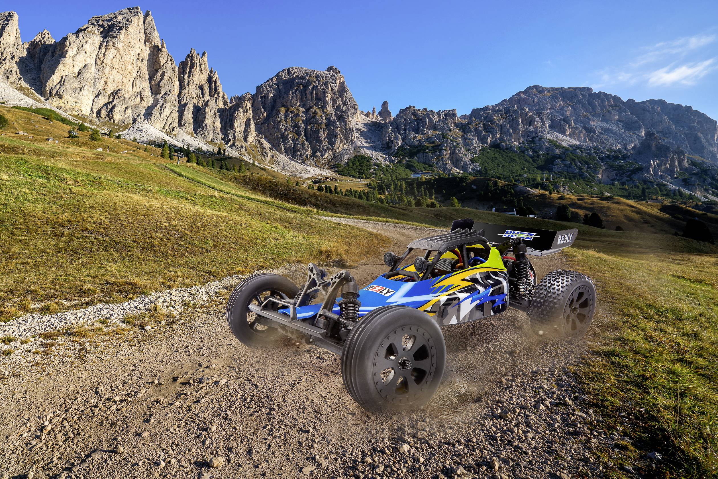 Ein blau-gelbes ferngesteuertes Auto fährt über eine staubige, unbefestigte Straße in einer gebirgigen Landschaft bei Sonnenschein.