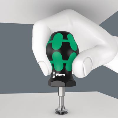 Eine Hand hält einen Schraubendreher der Marke Wera mit einem grün-schwarzen Griff und einem angebrachten Bit vor einer neutralen Hintergrundkulisse.