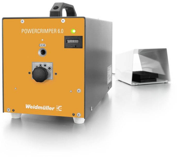 Ein oranger 'Powercrimper 6.0' von Weidmüller steht auf einem Tisch. Rechts daneben befindet sich eine metallische Abdeckung.