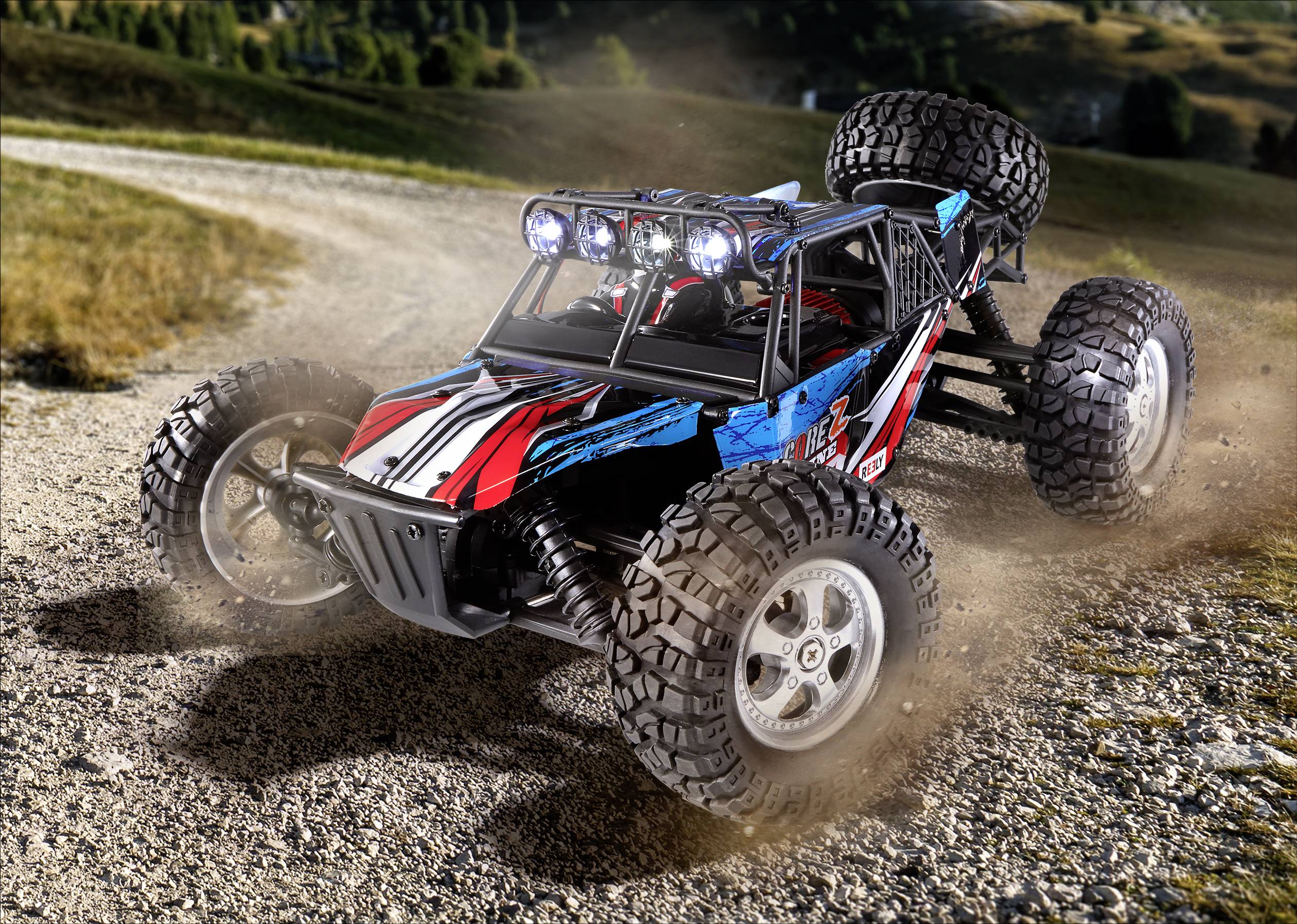 Spielzeug-Geländewagen mit großen Reifen fährt auf einem staubigen Pfad. Landschaft im Hintergrund, Lichter leuchten vorne.