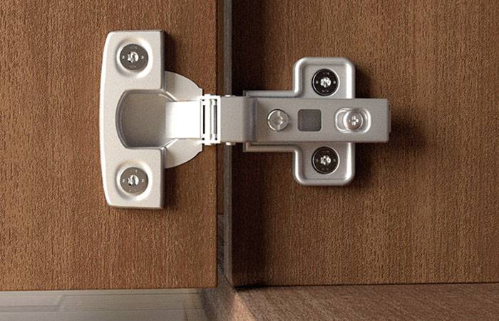 Ein Metallscharnier verbindet einen Holzschrank mit einer Tür. Scharnier ist silbern und befestigt, ermöglicht reibungslose Türbewegung.