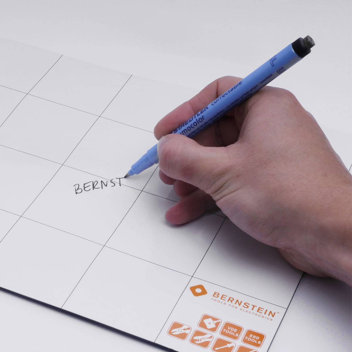 Eine Hand schreibt mit einem blauen Stift das Wort 'BERNST' auf eine weiße Tafel mit Raster. Unten rechts ist das Bernstein-Logo sichtbar.