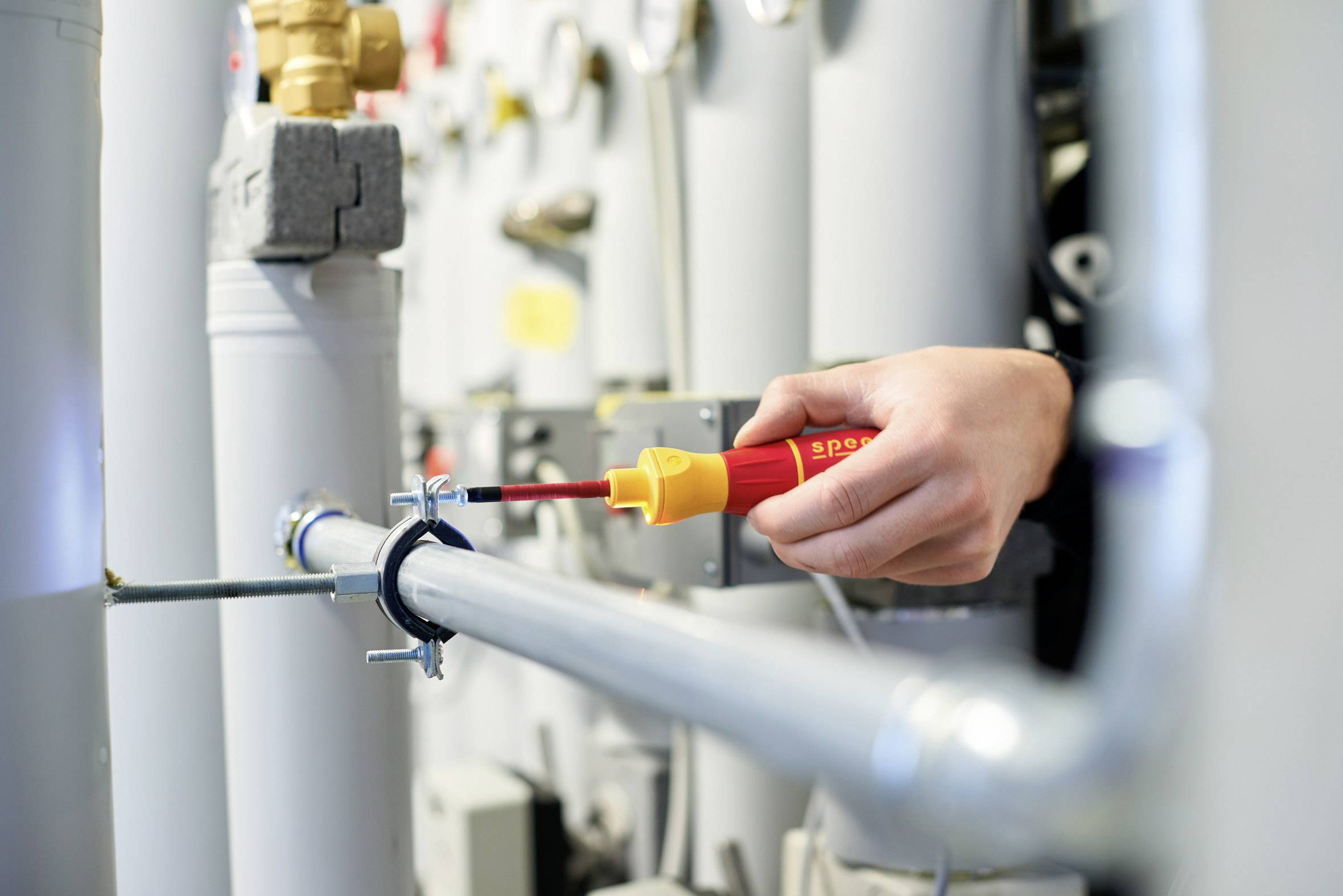 Eine Hand verwendet einen Schraubendreher, um eine Schelle an einem Rohr in einer industriellen oder technischen Umgebung zu befestigen.