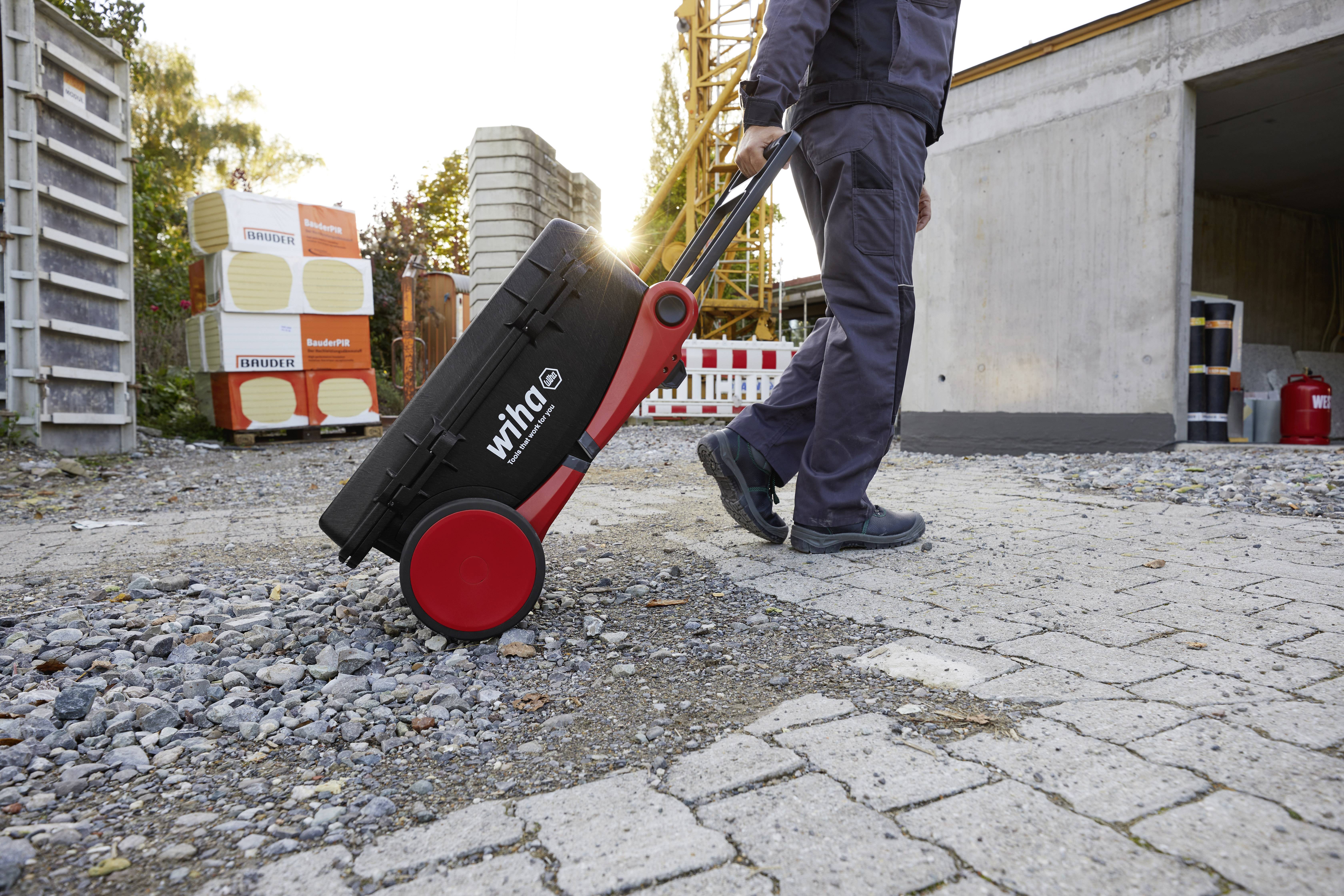 'Person zieht einen Werkzeugkoffer auf Rollen über eine Baustelle.'