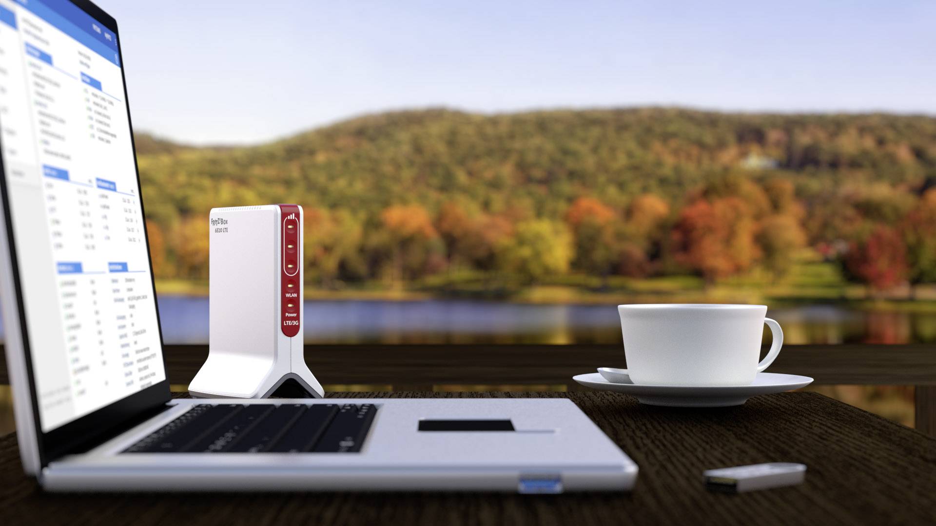 Ein Laptop und ein Router stehen auf einem Tisch im Freien mit einer Tasse Kaffee. Im Hintergrund ist eine herbstliche Landschaft sichtbar.