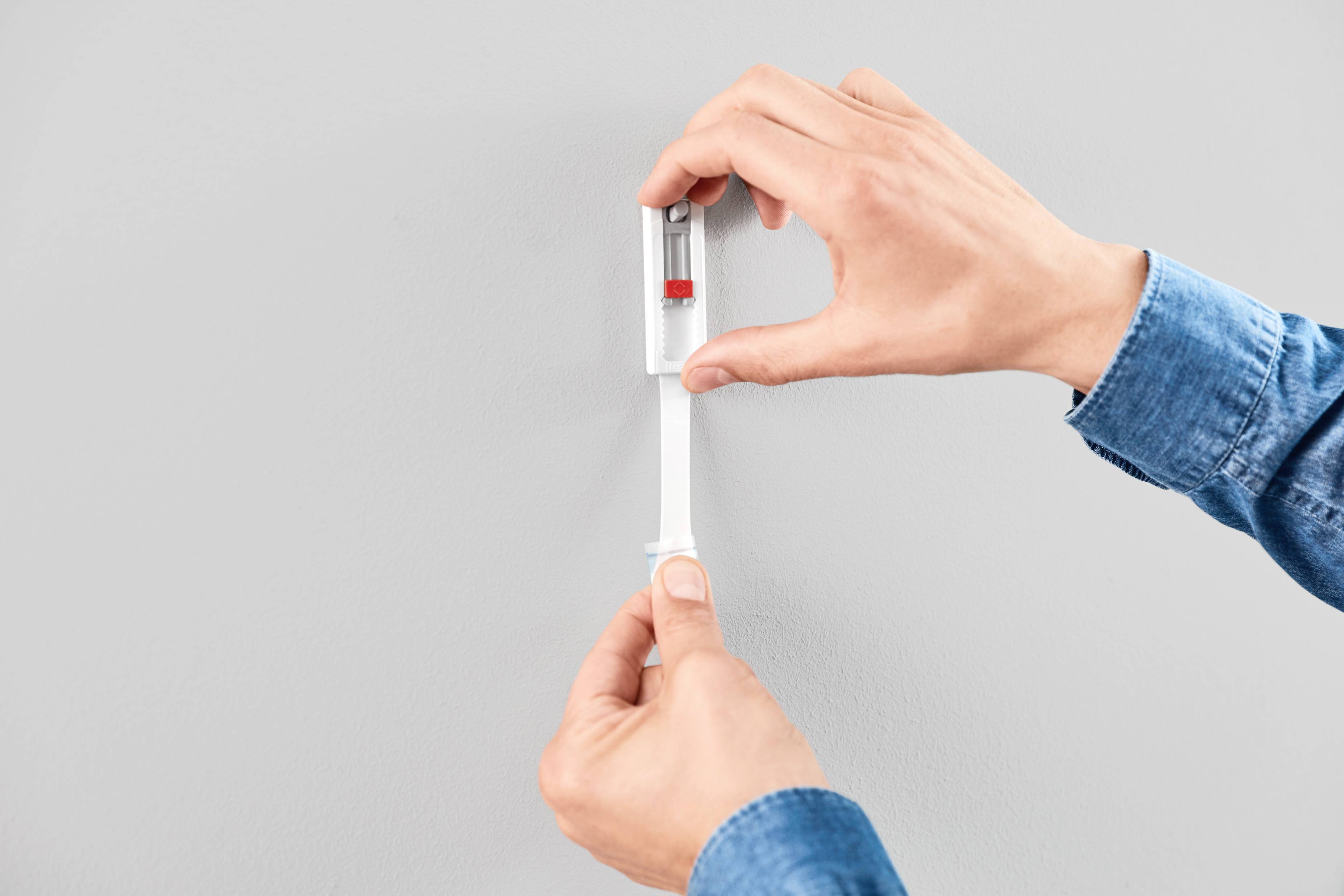 Zwei Hände, die ein Wasserwaagenwerkzeug an einer hellgrauen Wand halten, um die horizontale Ausrichtung zu überprüfen.