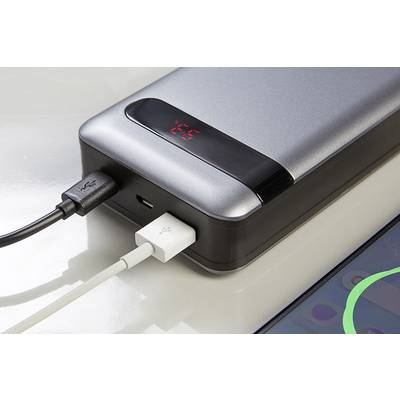 Eine Powerbank lädt ein Smartphone. Zwei Kabel sind angeschlossen; eins zeigt auf ein nahegelegenes Smartphone mit aktiviertem Display.