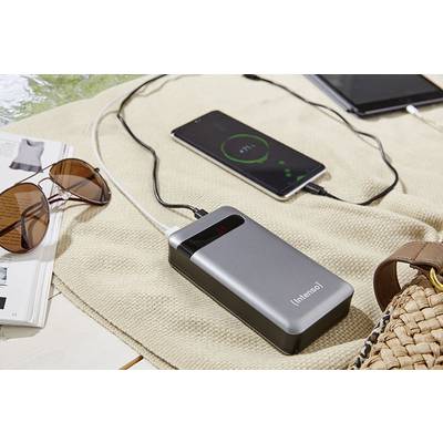 Tragbare Powerbank lädt Smartphone auf. Ein Tablet, eine Sonnenbrille und ein offenes Magazin liegen daneben auf einer Decke.
