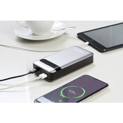 Eine Powerbank lädt zwei Geräte auf einem Tisch auf: ein Smartphone mit 71% Ladung und ein Tablet. Im Hintergrund eine Tasse.