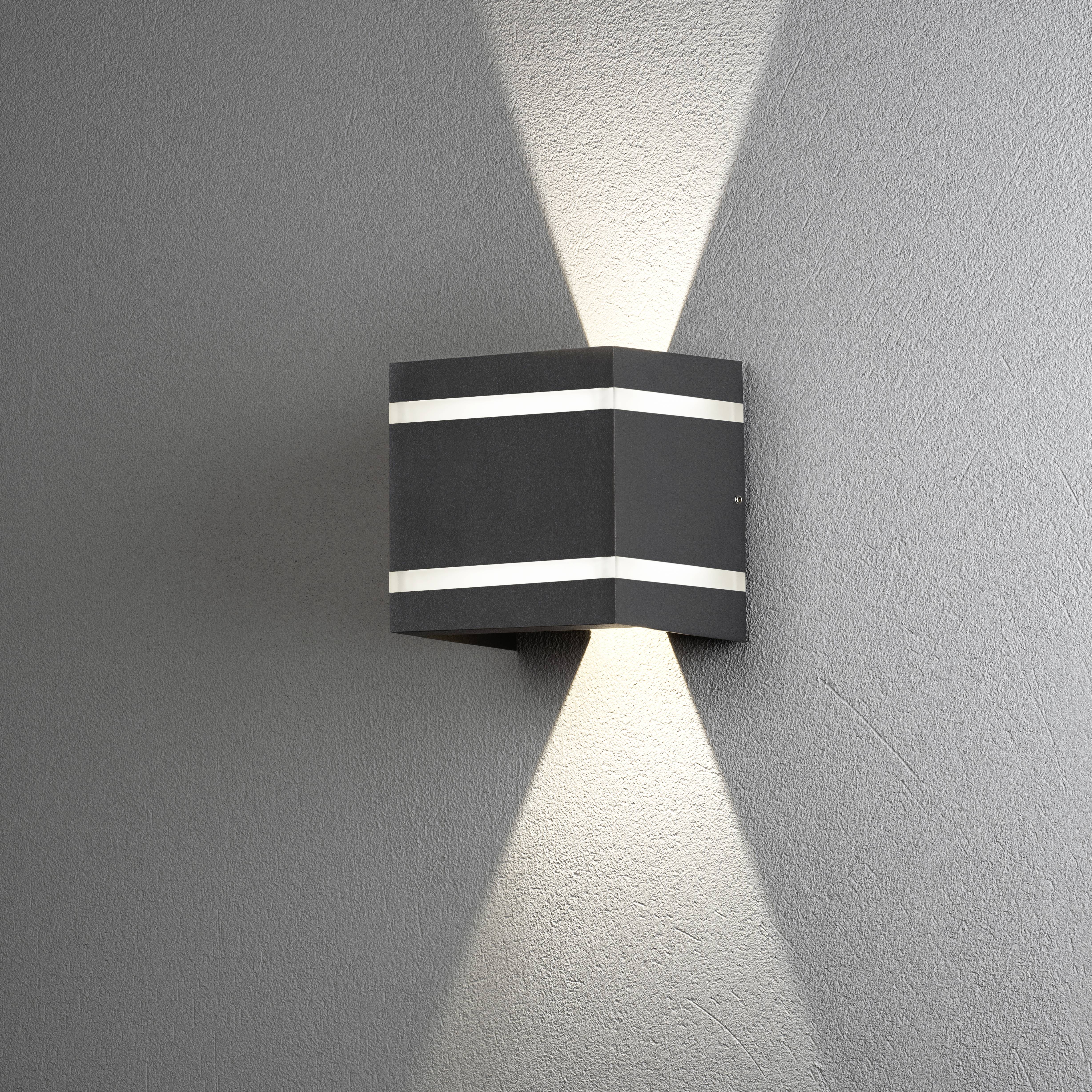 Schwarze Wandleuchte mit zwei horizontalen Lichtstreifen; strahlt nach oben und unten, erzeugt dekorativen Lichteffekt an grauer Wand.