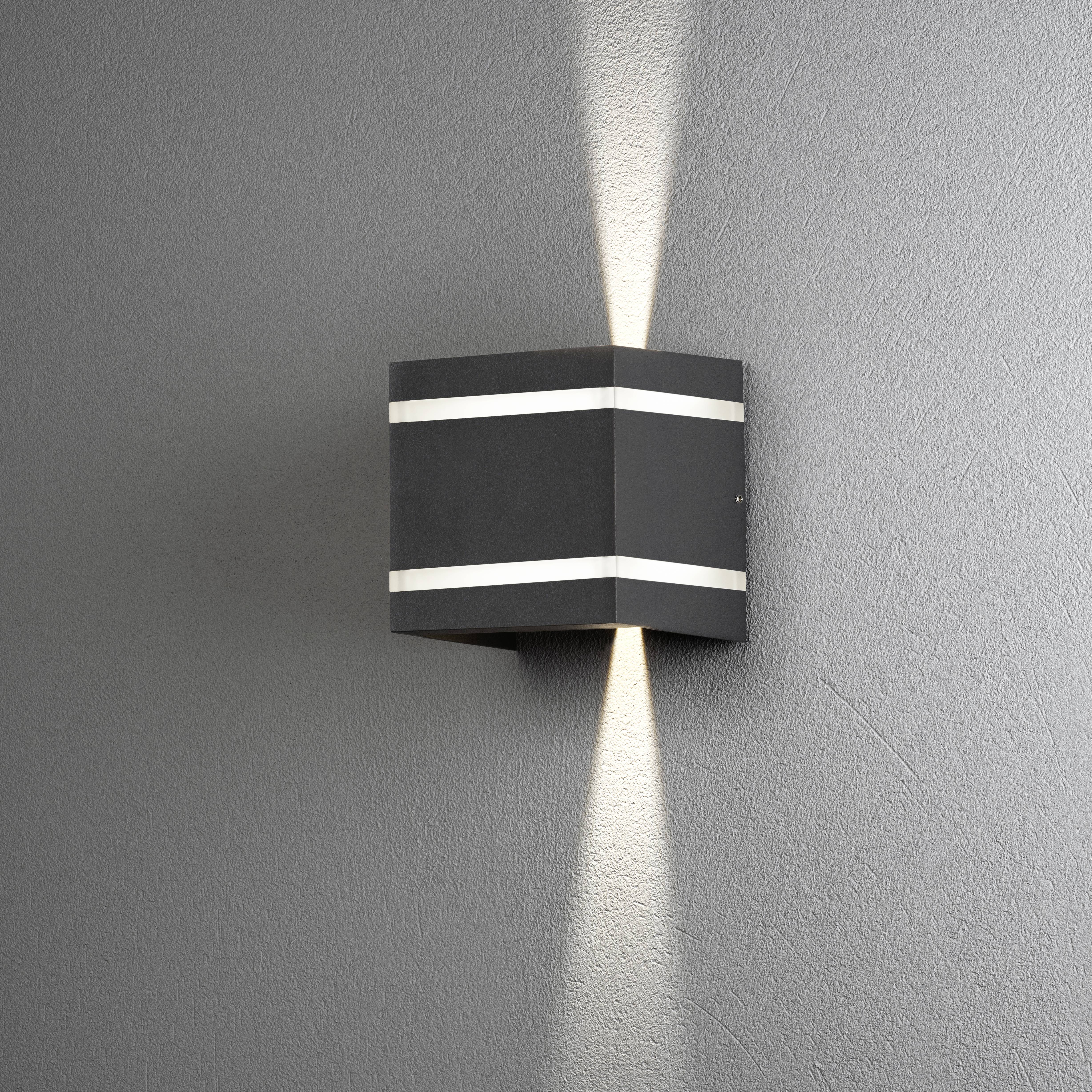 Wandlampe mit modernem, eckigem Design leuchtet nach oben und unten. Schlichtes Ambiente an grauer Wand.