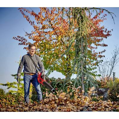 Ein Mann benutzt einen Laubbläser, um Herbstlaub in einem Garten wegzublasen. Im Hintergrund sind bunte Herbstbäume zu sehen.