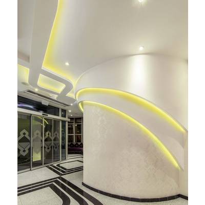 Modernes Foyer mit geschwungenen Wänden und gelben LED-Lichtern. Schwarz-weißes geometrisches Bodenmuster und Glastüren links.