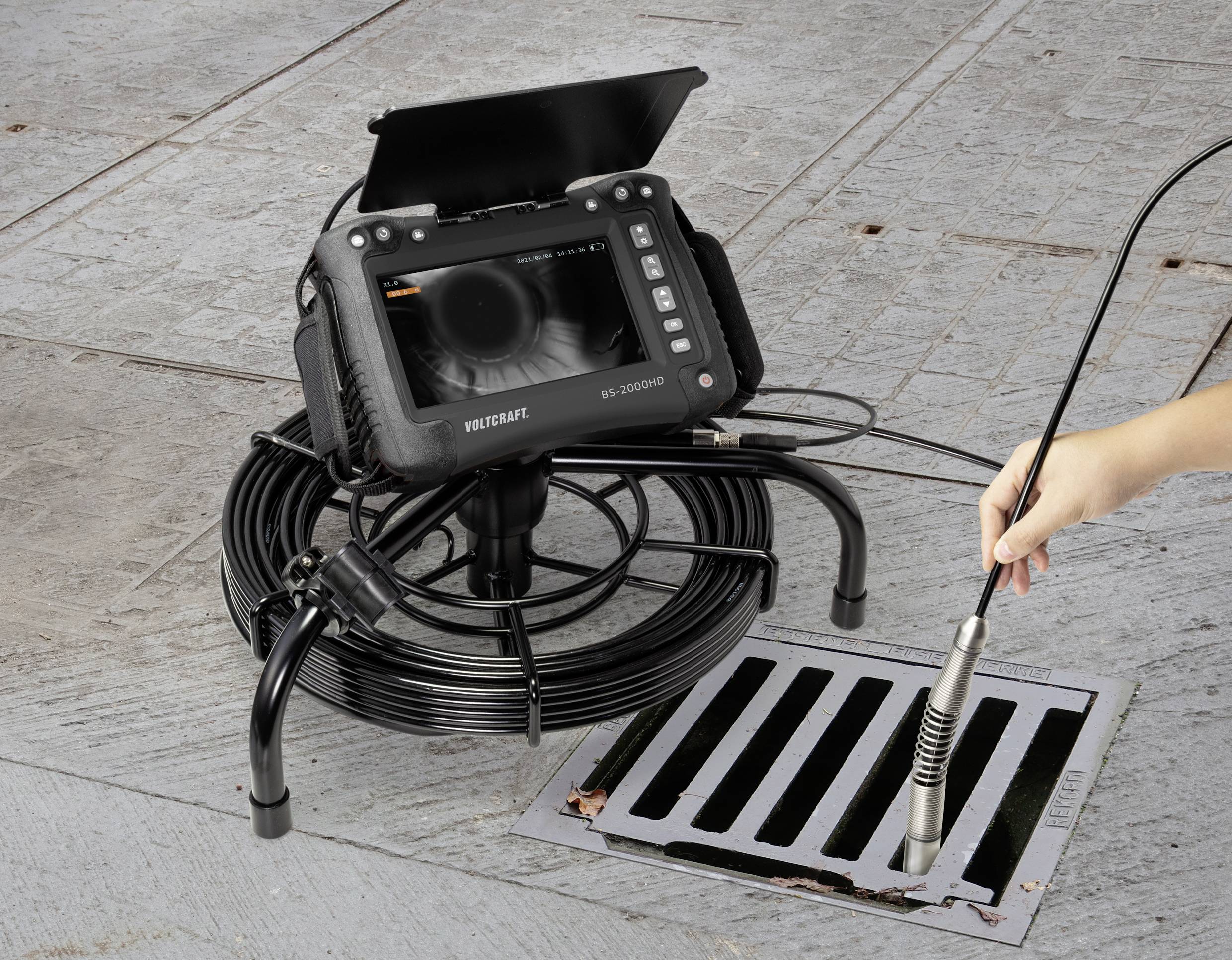 'Inspektionskamera über einem Gitter, ein Rohr in den Abfluss führend, zeigt abgetastete Bilder auf einem Monitor.'