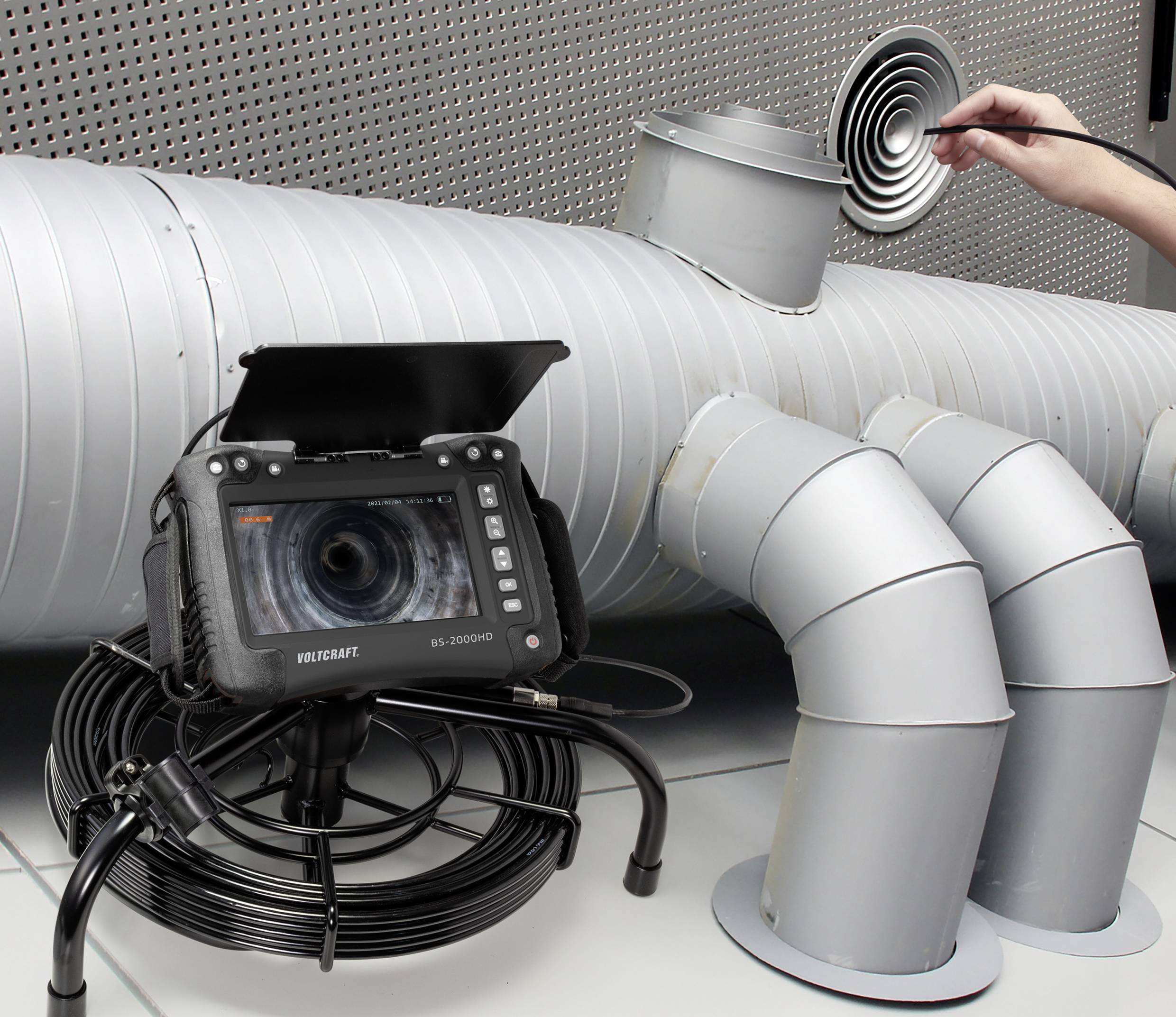 Eine Person inspiziert mit einem Schallkamera-System eine Lüftungsanlage. Es zeigt die Kamera auf einem Bildschirm und Lüftungsrohre.