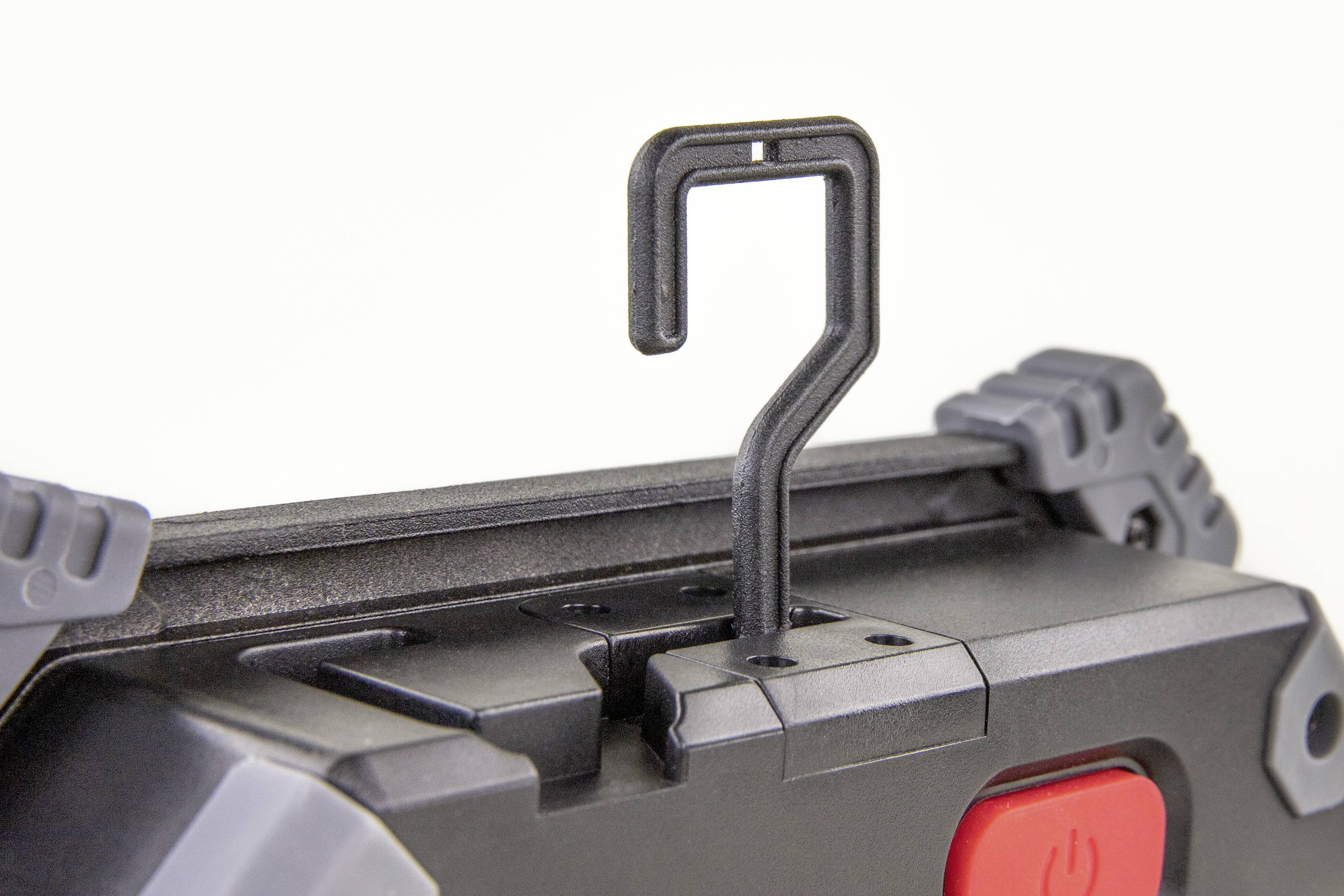 Ein Haken an einem schwarzen Gehäuse mit grauen Ecken und rotem Knopf, möglicherweise Teil eines Ausrüstungsgegenstands oder Werkzeugs.