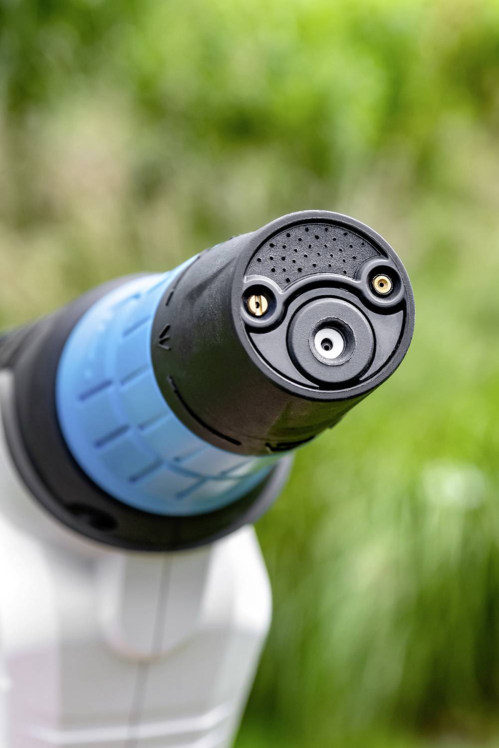 Nahaufnahme eines blauen Akkuschraubers mit schwarzem Kopf, dargestellt vor einem unscharfen, grünen Hintergrund im Freien.