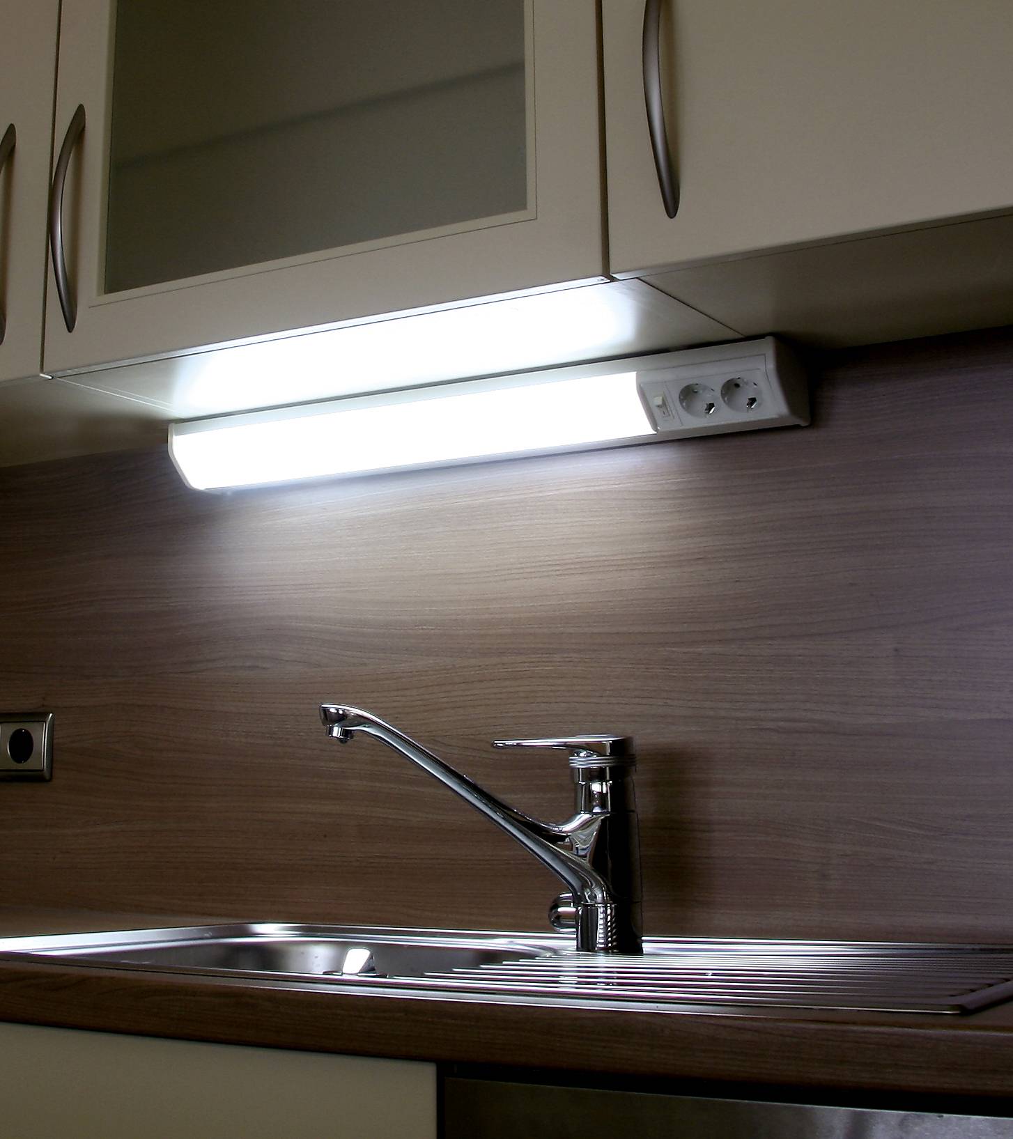 Küchenarbeitsfläche mit Edelstahlspüle und modernem Wasserhahn, darüber ein Unterbauleuchtmittel, sorgt für optimale Ausleuchtung.
