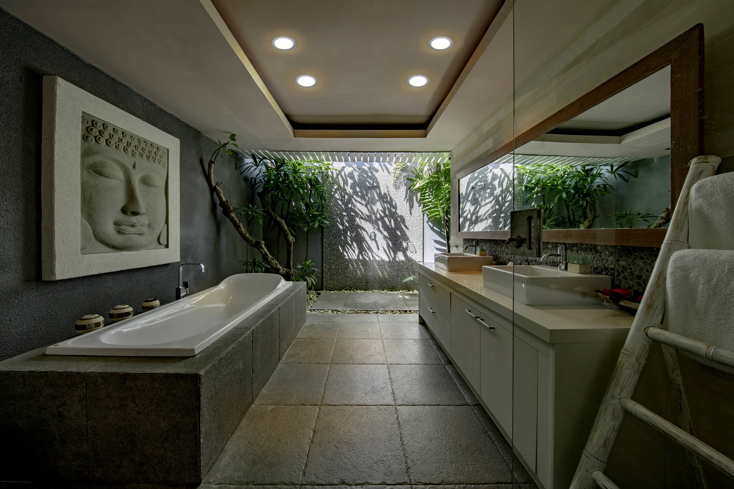 Luxuriöses Badezimmer mit moderner freistehender Badewanne, großem Spiegel, hölzernem Wandkunstwerk und Pflanzen im Außenbereich.