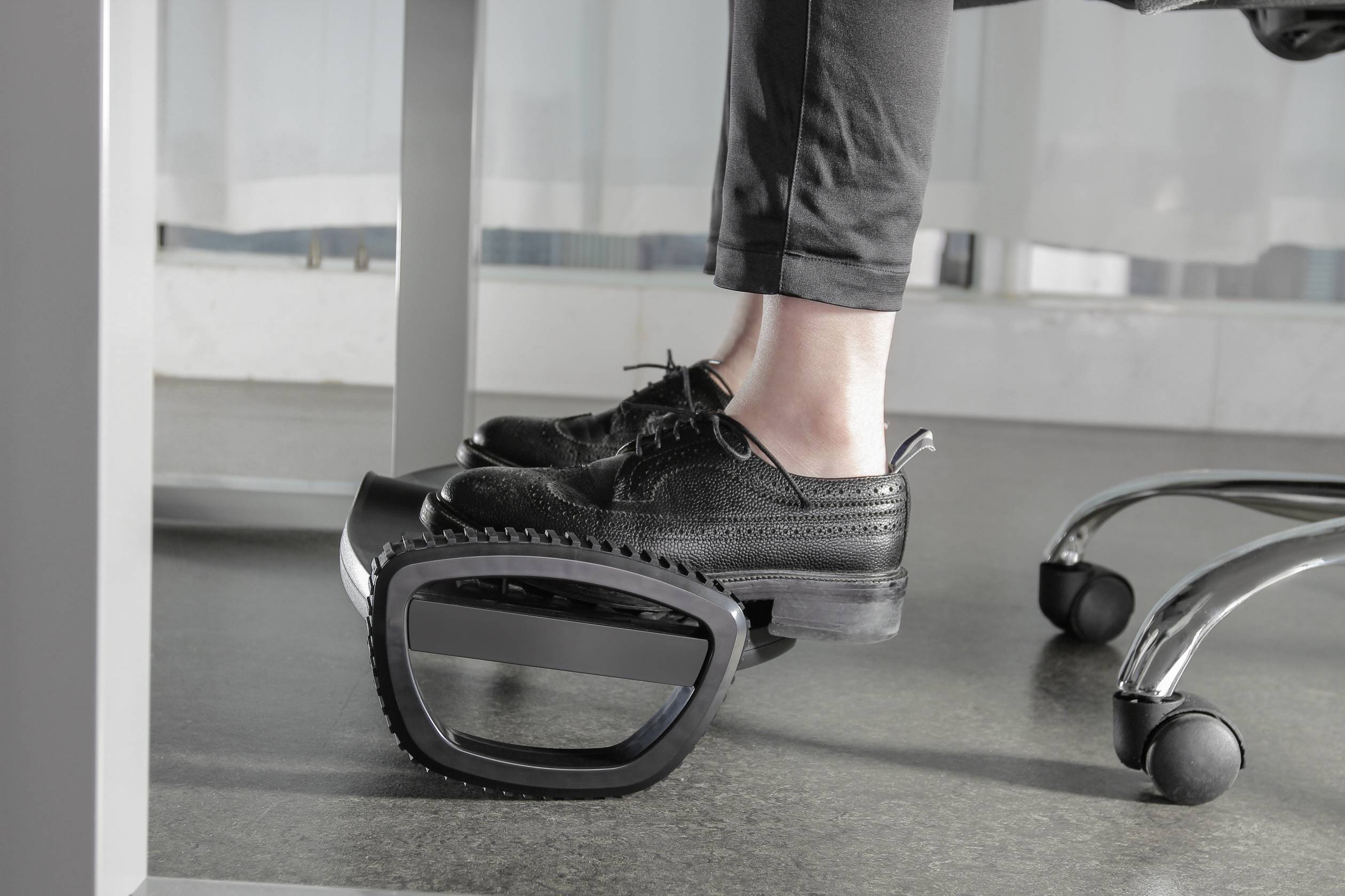 Eine Person sitzt an einem Schreibtisch und nutzt eine ergonomische Fußstütze, um die Füße zu unterstützen und den Komfort zu erhöhen.
