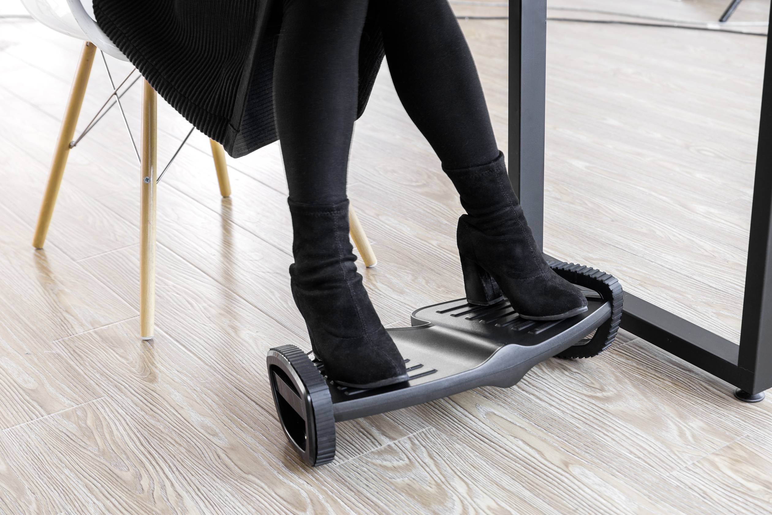 Person mit schwarzen Stiefeln nutzt ein Büro-Fitnessgerät unter einem Schreibtisch, um die Füße in einer sitzenden Position zu bewegen.
