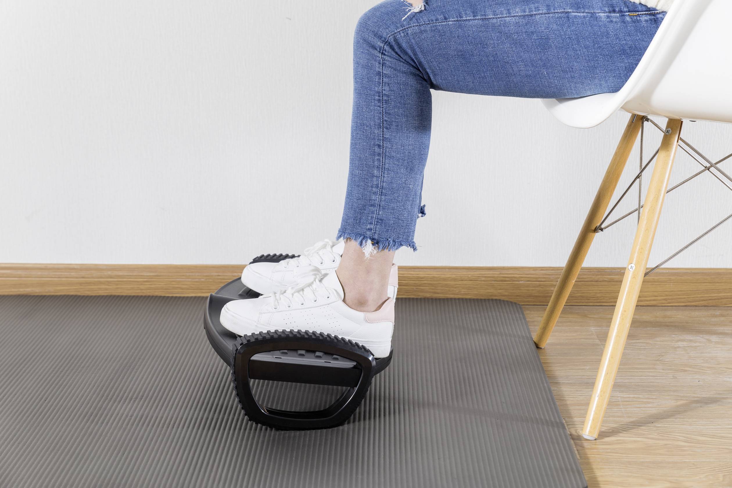 Eine Person in Jeans und weißen Turnschuhen benutzt eine Fußstütze, während sie auf einem weißen Stuhl sitzt.