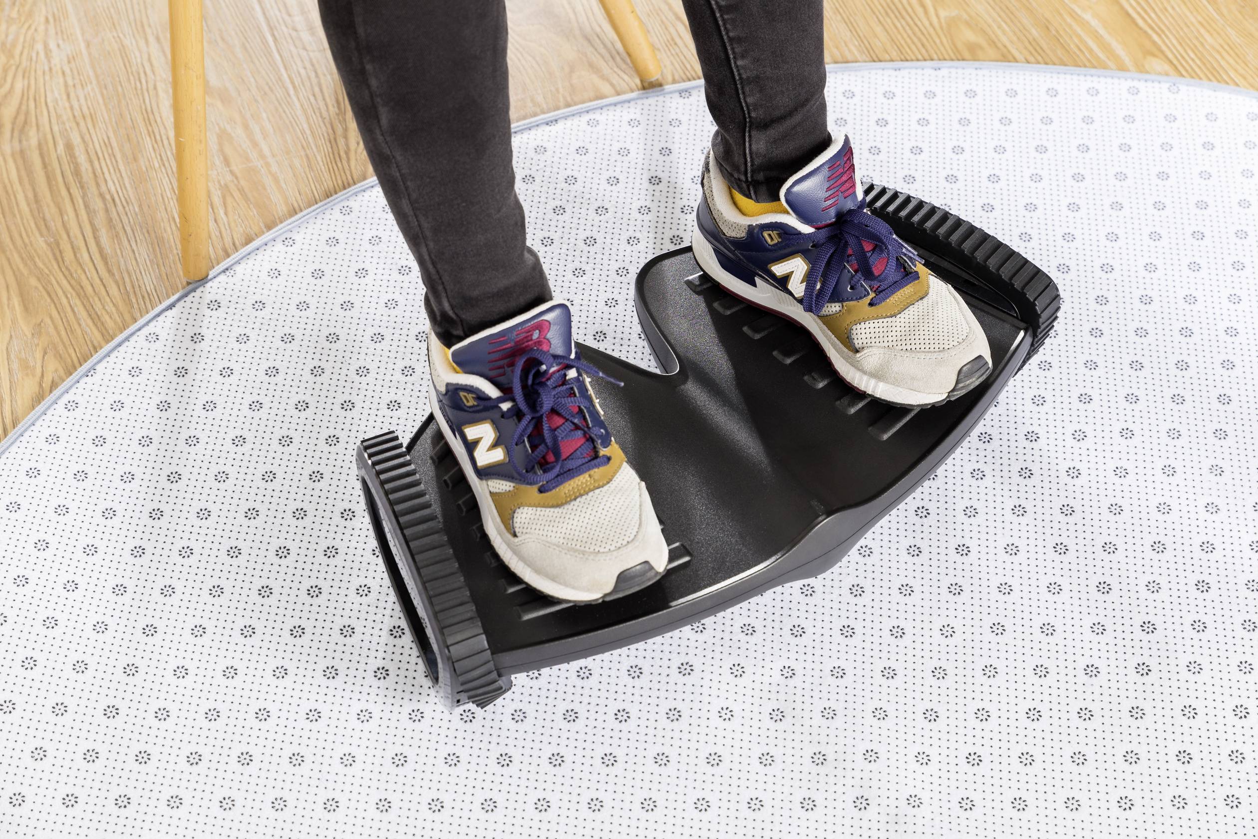 Jemand steht mit Sportschuhen auf einem schwarzen Balance-Trainingsgerät auf einem gepunkteten Teppichboden.