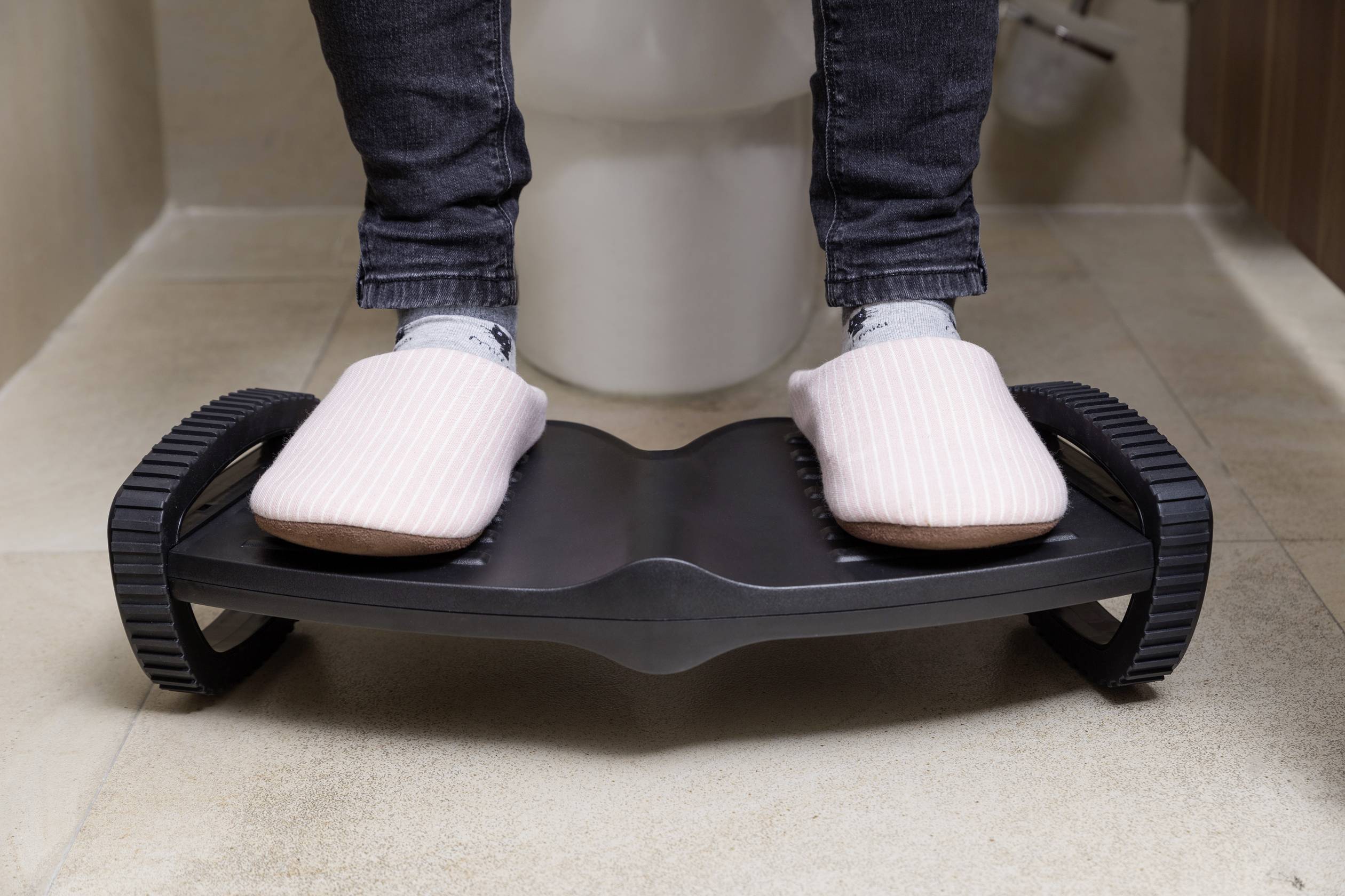 Person mit rosa Hausschuhen steht auf Fußstütze im Badezimmer.
