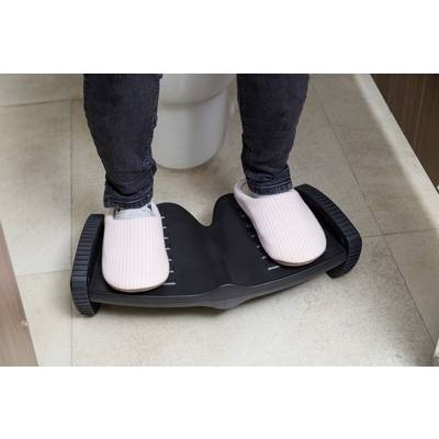 Eine Person steht auf einer schwarzen Balance-Plattform, trägt rosa Hausschuhe. Die Plattform hat gerillte Seiten und ist auf Fliesenboden.