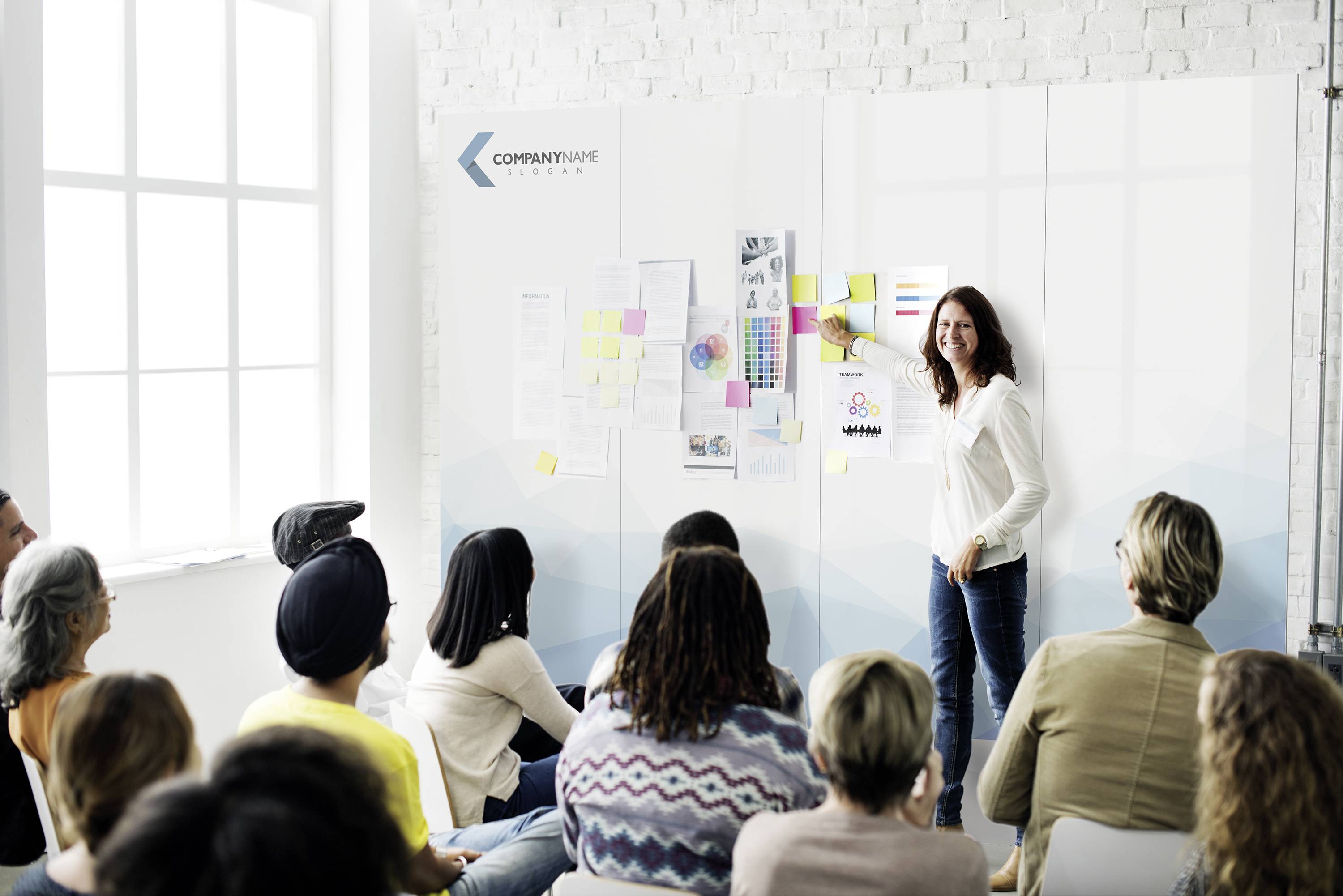 Eine Frau steht vor einer Gruppe, zeigt auf ein Whiteboard mit Grafiken und Notizen. Sie hält eine Präsentation ab.