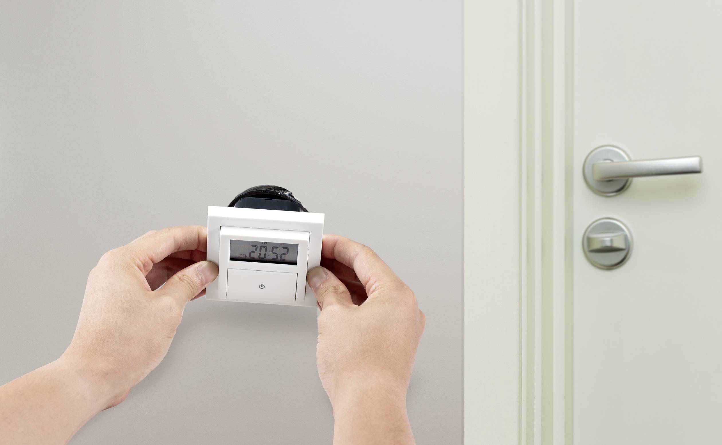 Eine Person installiert oder justiert einen Wandthermostat mit digitalem Display, das die Temperatur von 20,5 Grad Celsius anzeigt.