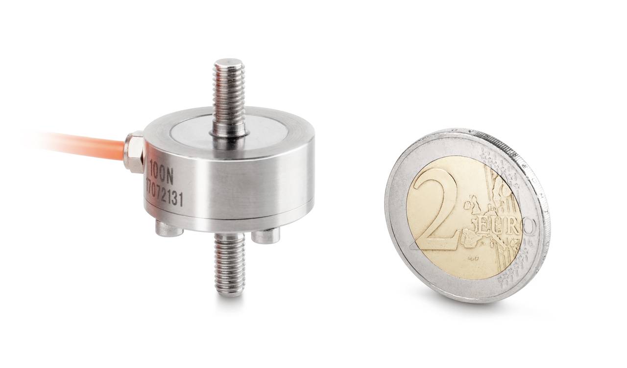 Kraftsensor in zylindrischer Form mit Kabelanschluss, daneben eine 2-Euro-Münze als Größenvergleich.