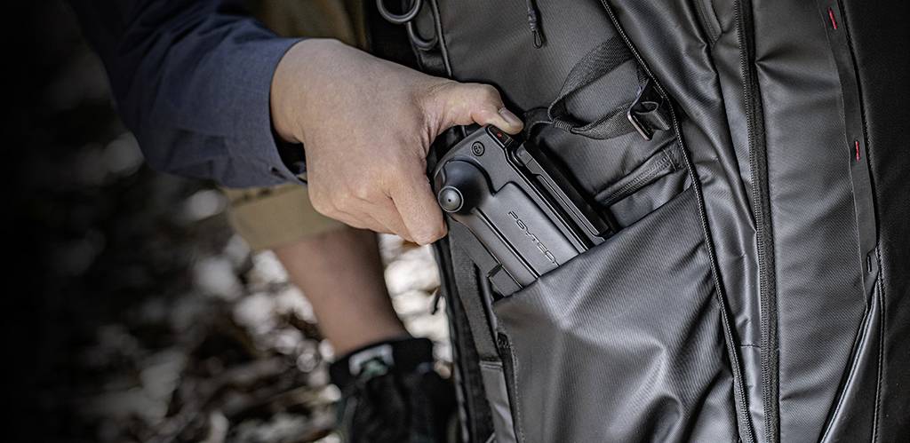 Eine Person steckt ein zusammenschiebbares Werkzeug in eine Seitentasche eines Rucksacks. Das Werkzeug hat einen drehbaren Griff.